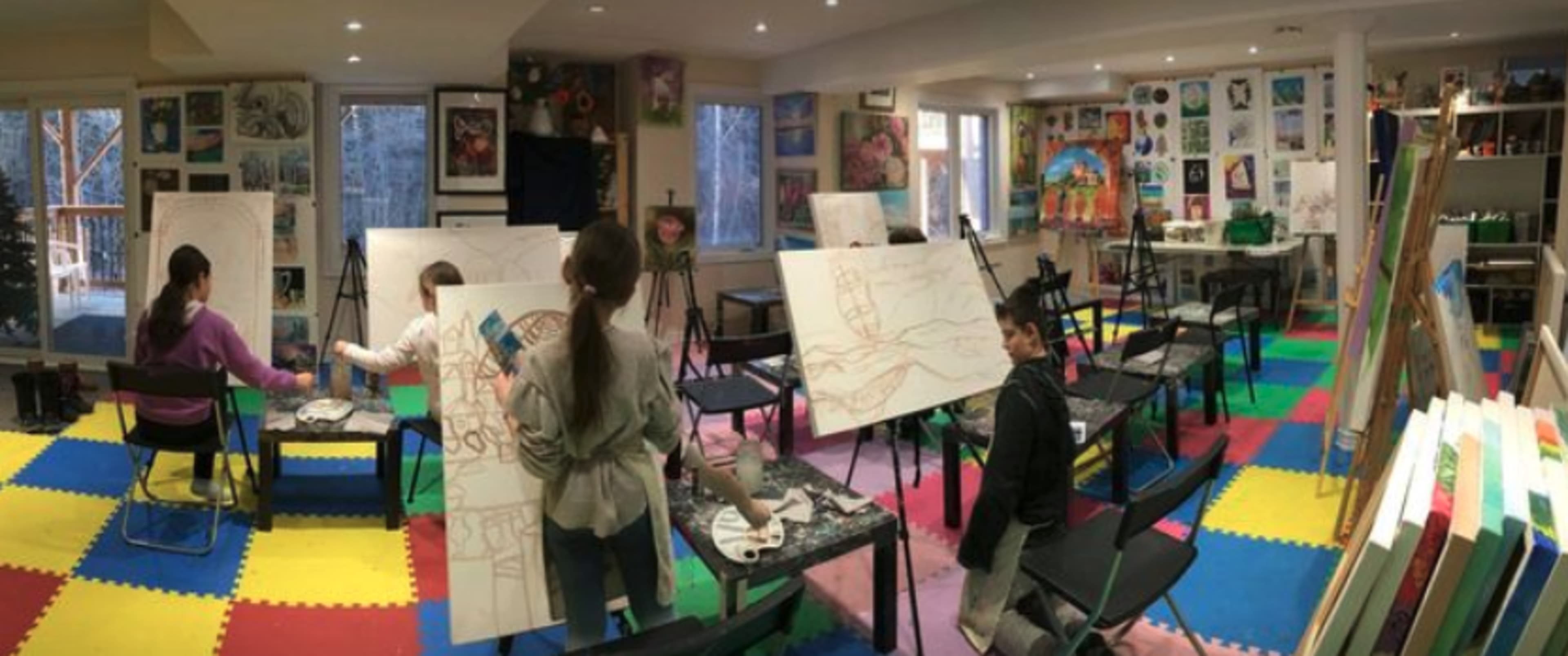 A group of artists is working on large canvases in a colorful studio surrounded by various finished artworks.