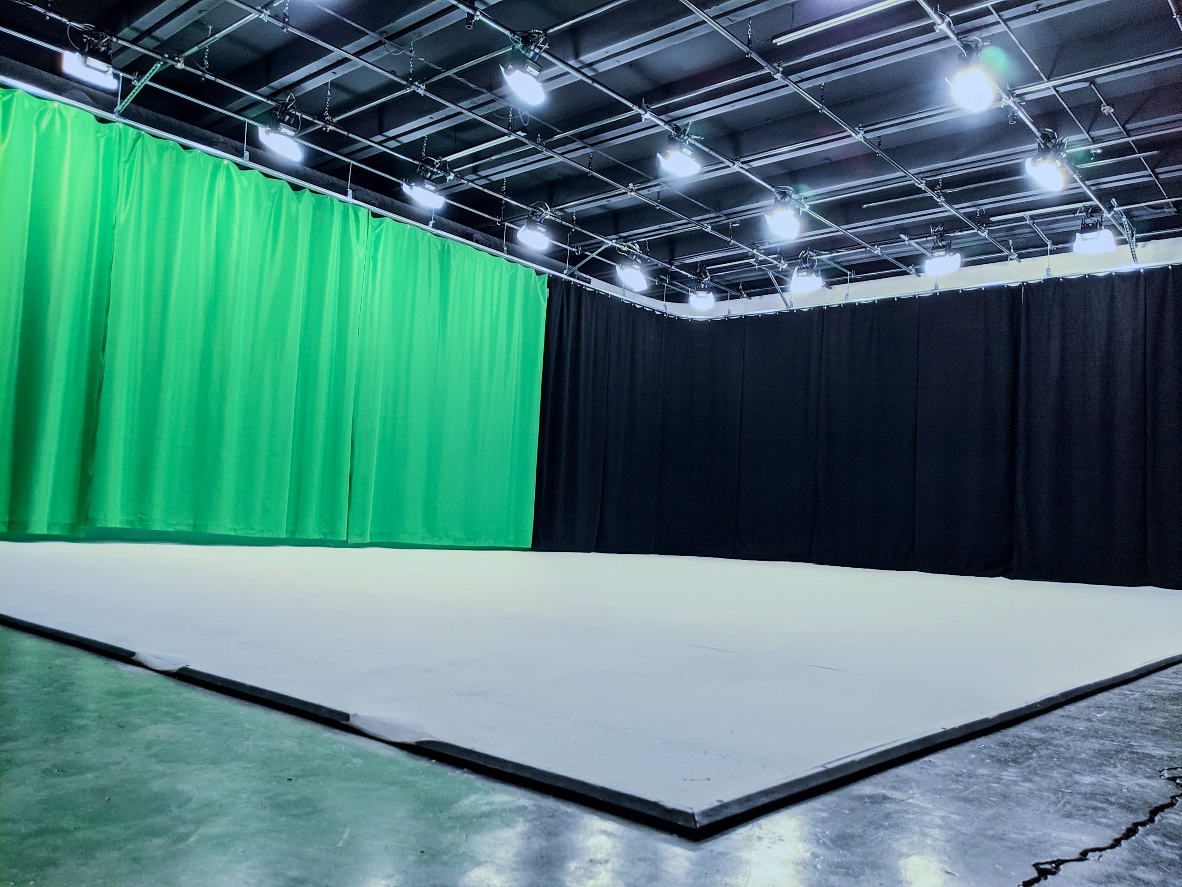 The image shows a studio space with a green screen curtain on one side and black curtains on the other, set against a plain floor.