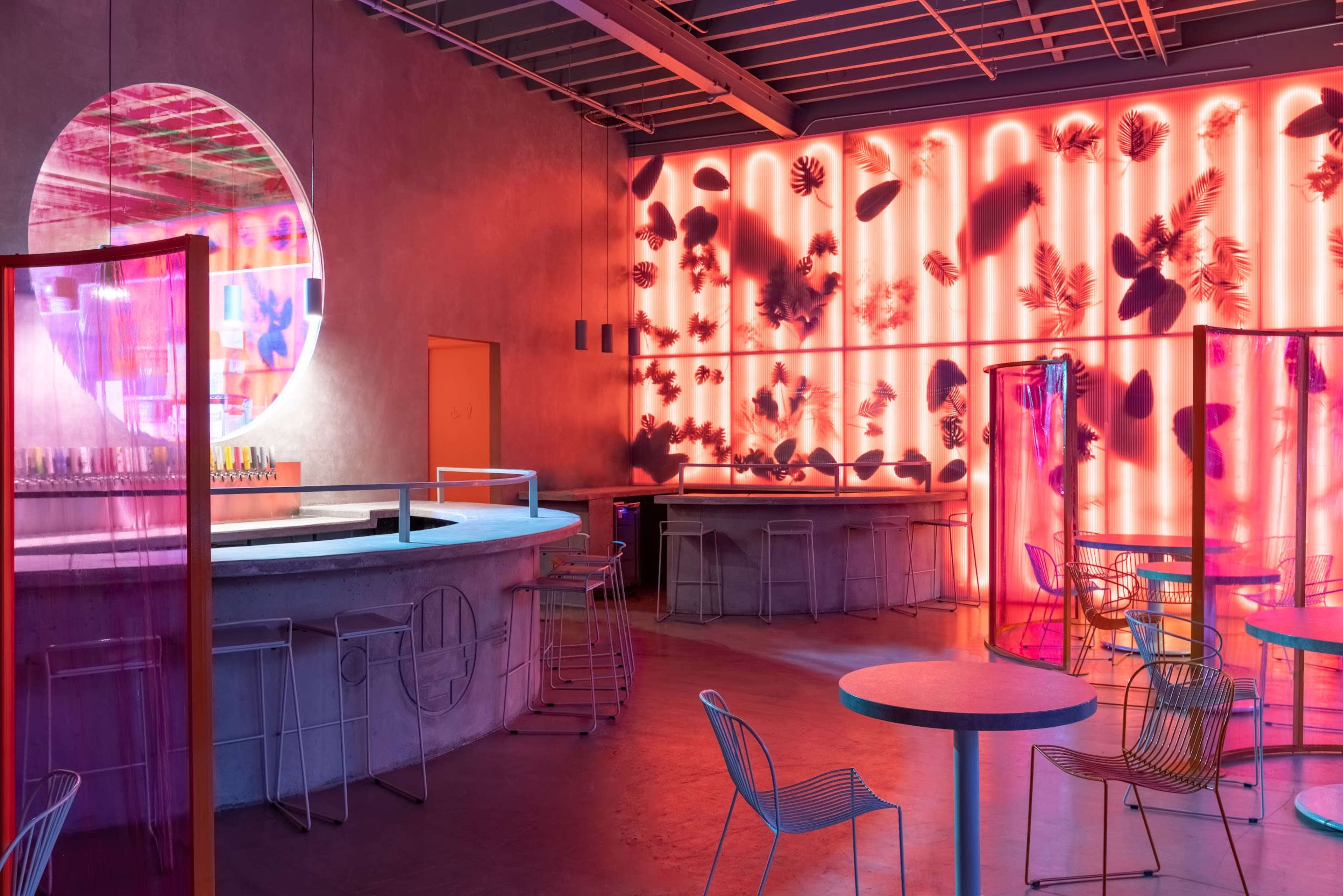 A modern bar interior with colorful lighting, circular mirrors, and a mix of seating arrangements.