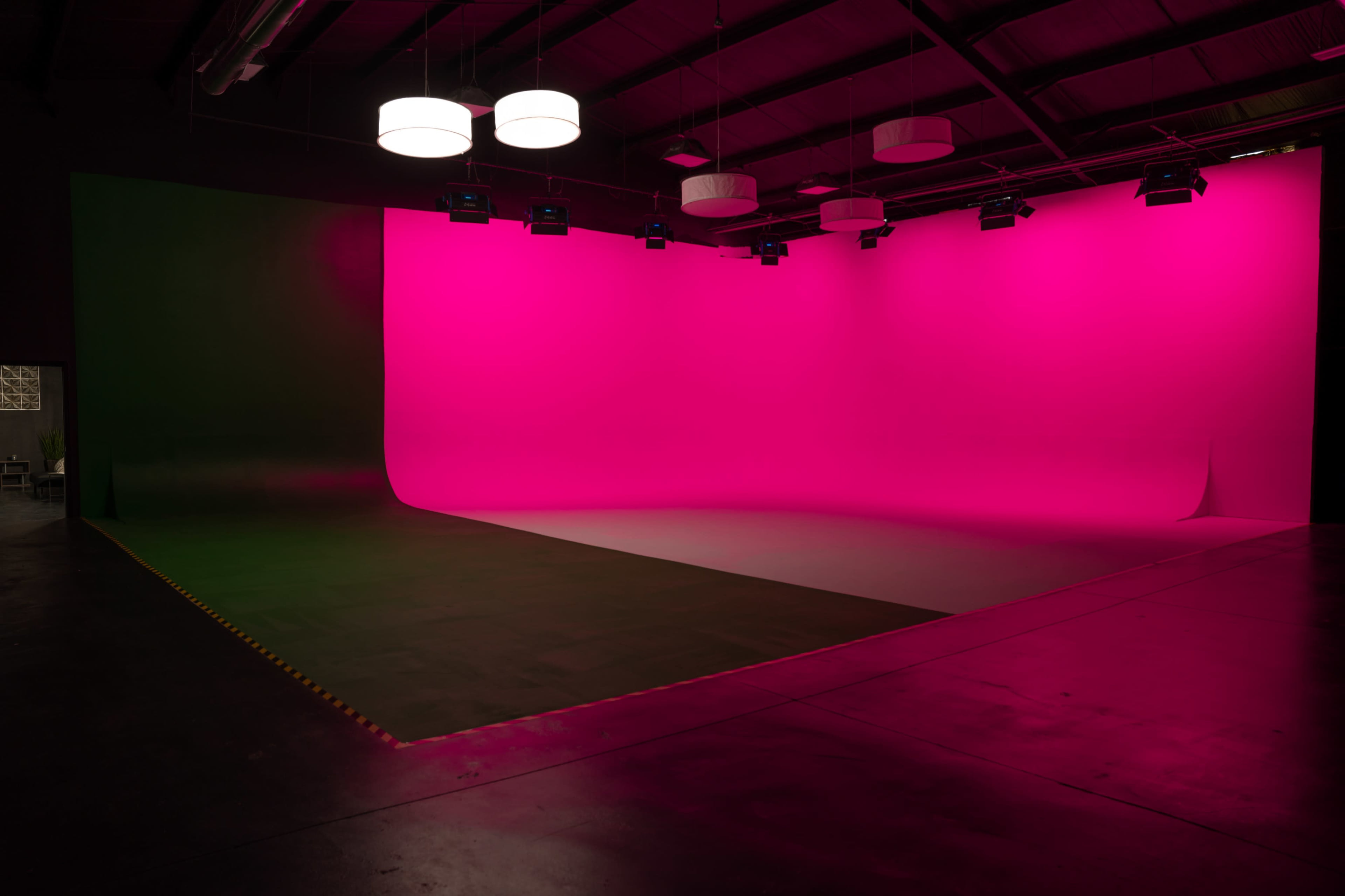 A studio space with a large curved pink backdrop and green walls, illuminated by overhead lighting.