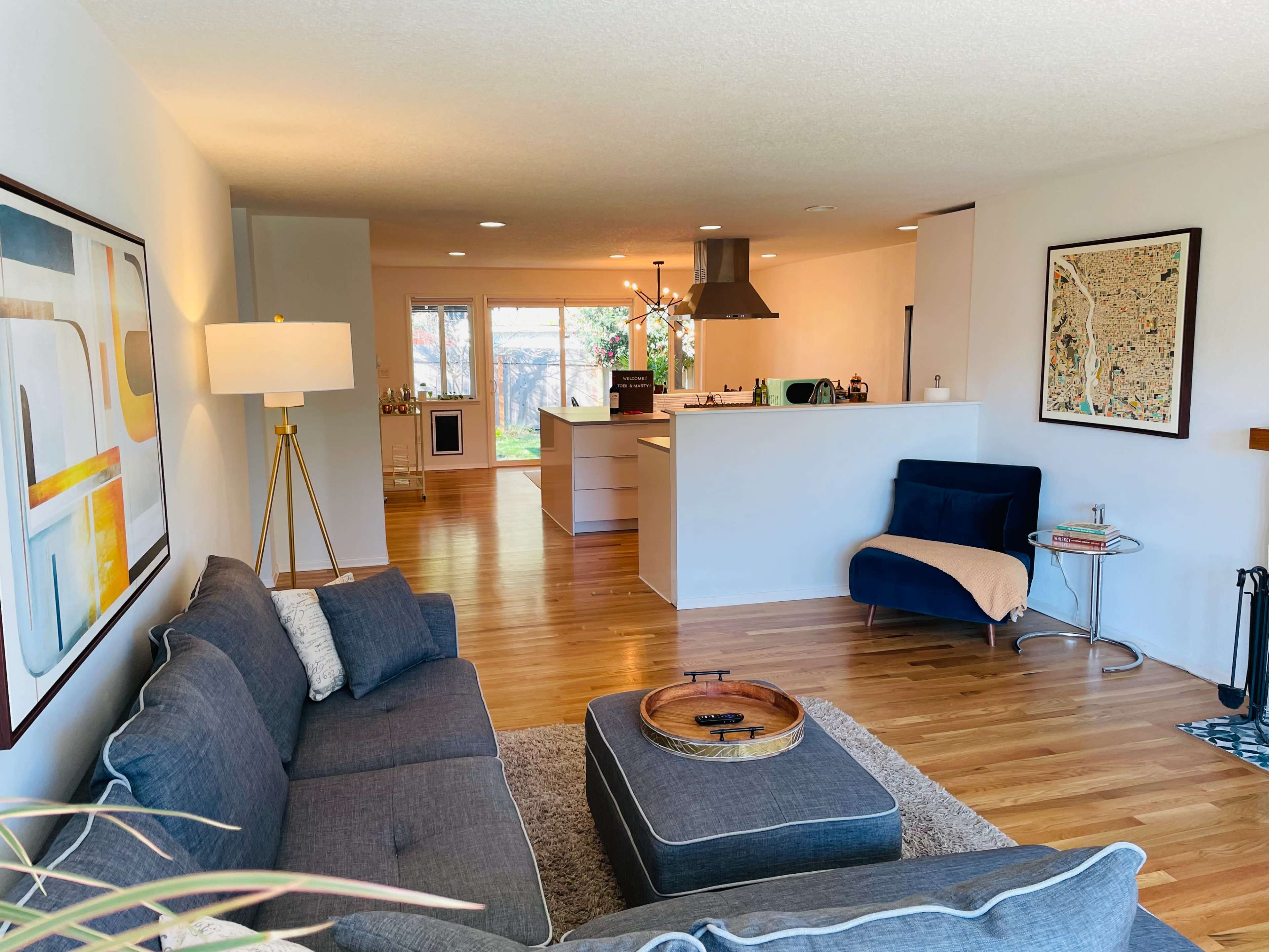 A modern living area featuring a gray sofa, a round coffee table, and a view of a kitchen in the background with large windows providing natural light.