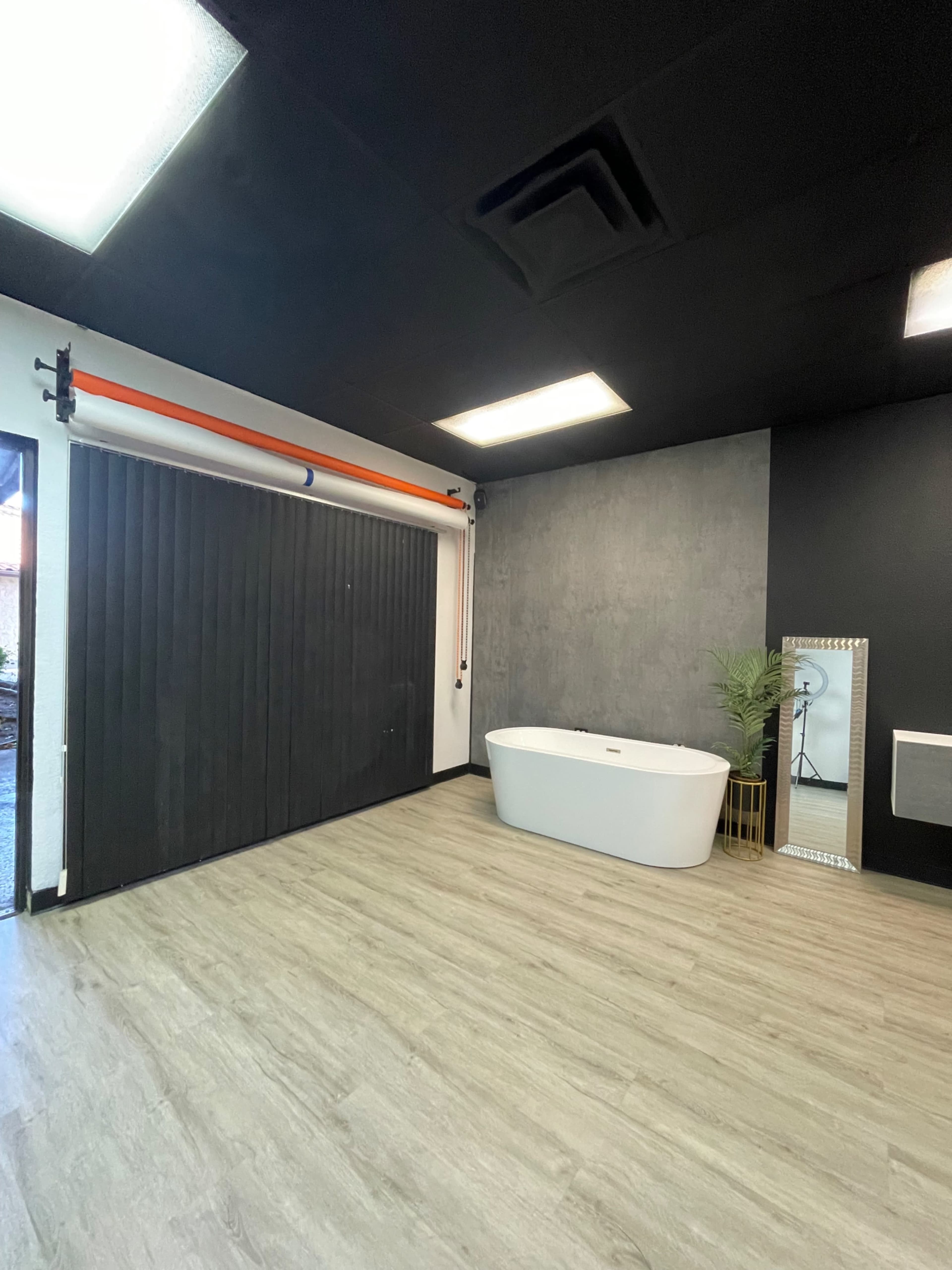 The image showcases a modern room featuring a freestanding bathtub, a large black sliding door, and a full-length mirror against a textured wall.