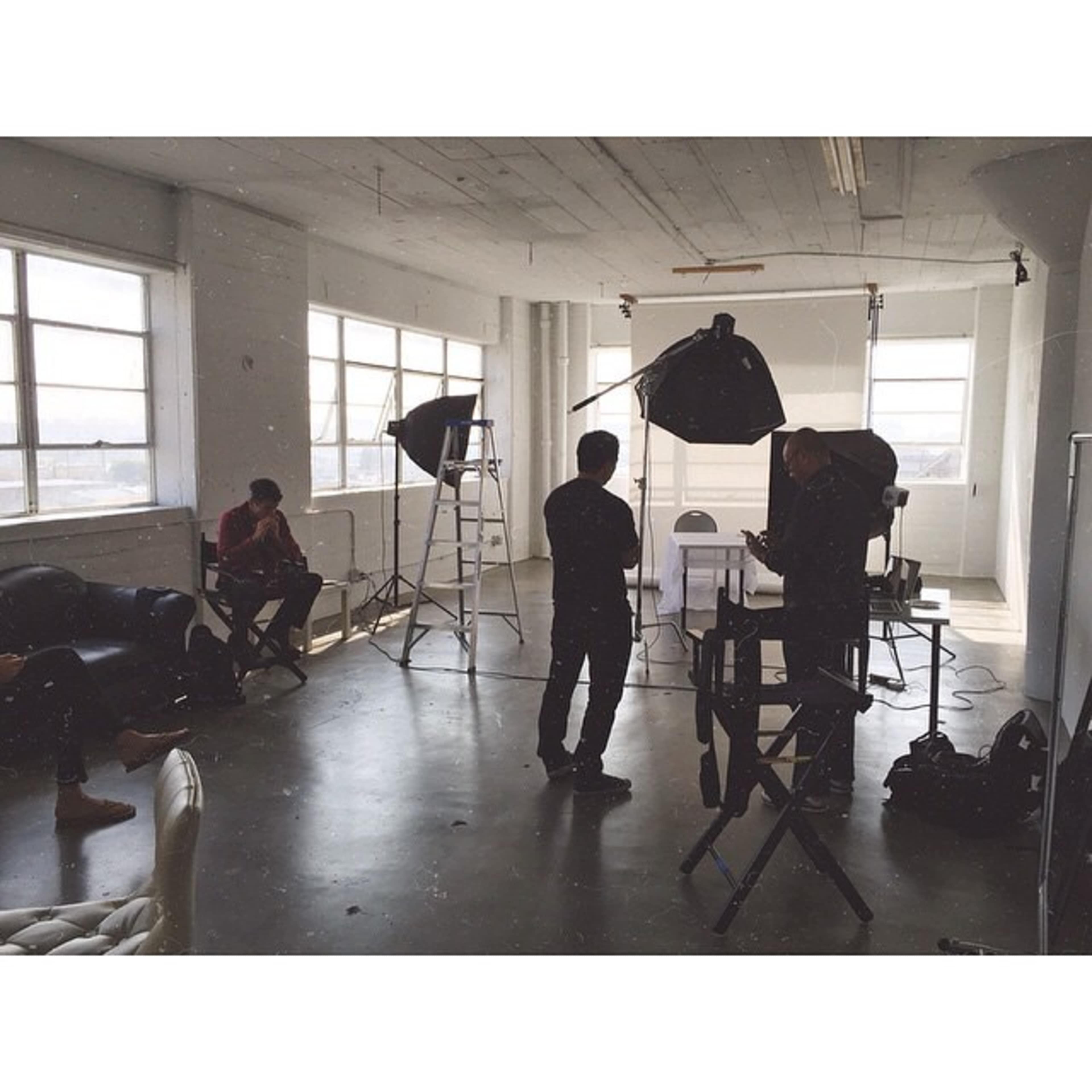 A photography studio setting with individuals preparing for a photoshoot, featuring lighting equipment and a backdrop.
