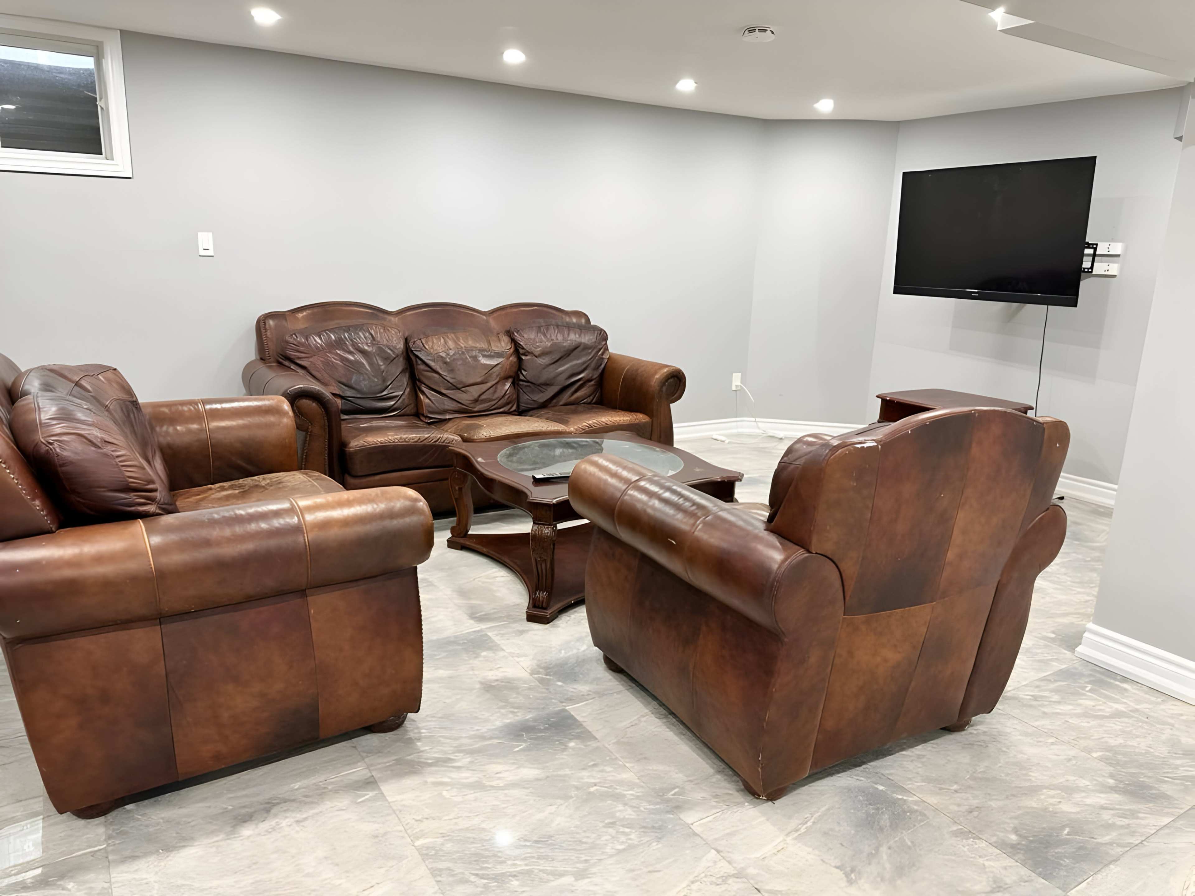A living room with brown leather couches, a wooden coffee table, and a wall-mounted television in a light grey setting.