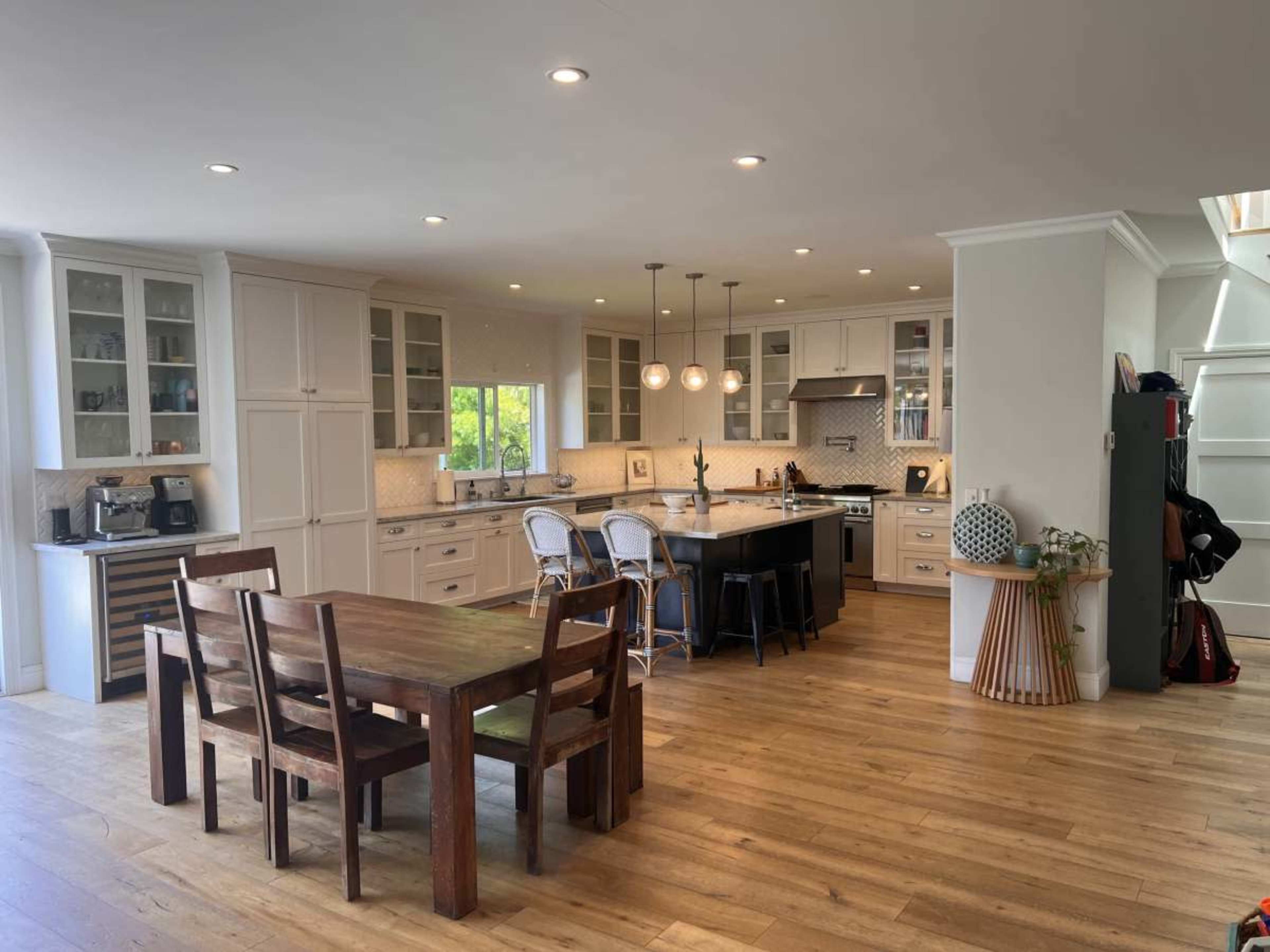 The kitchen features white cabinetry, a central island with bar seating, and a wooden dining table, illuminated by pendant lights.
