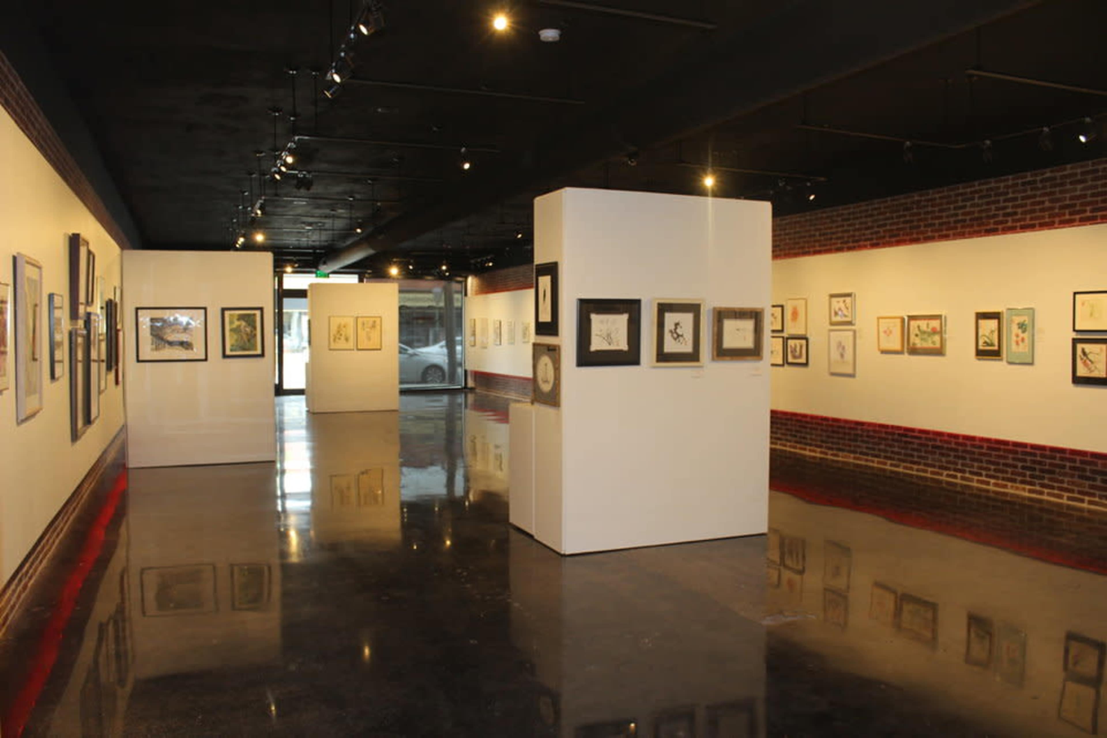 An art gallery with framed artworks displayed on white walls and a polished concrete floor.