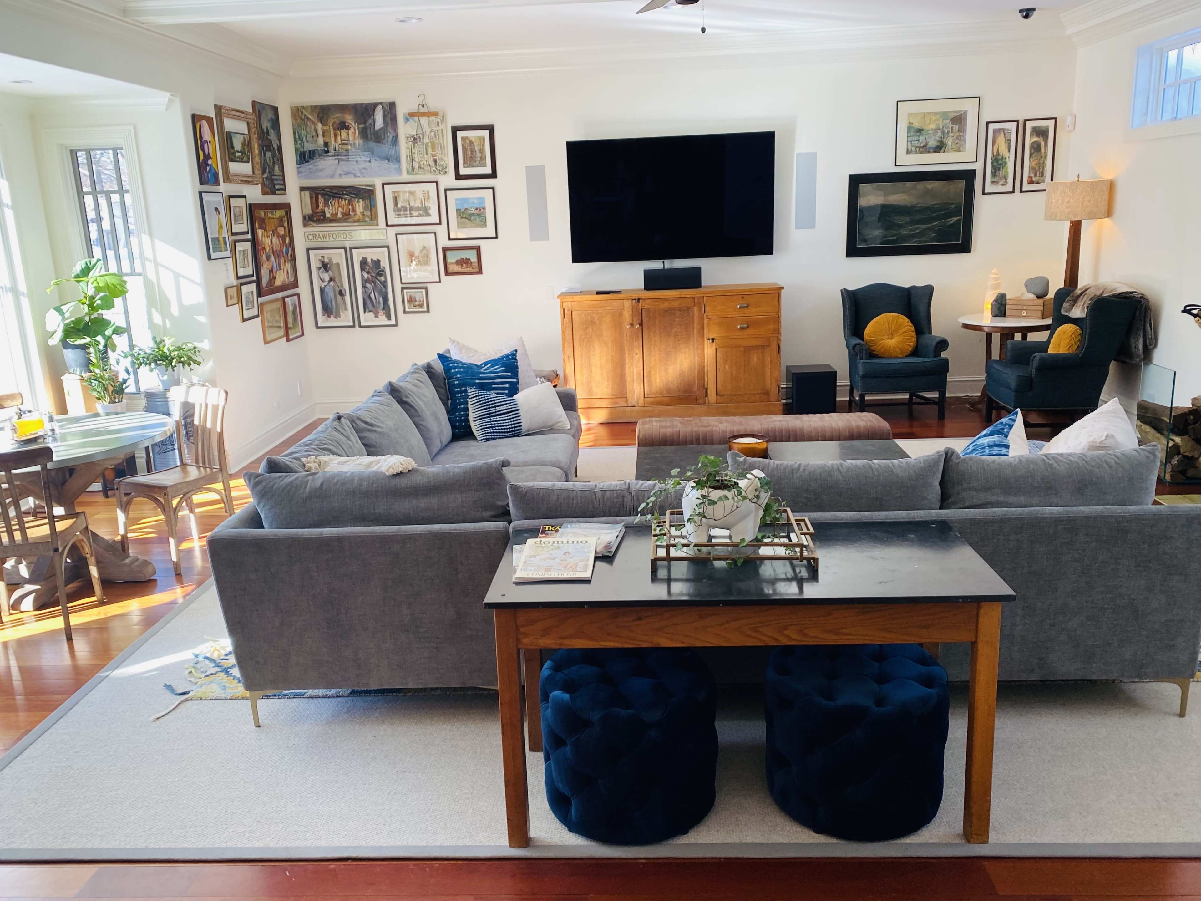 A spacious living room features a gray sectional sofa, a wooden coffee table with decorative items, and walls adorned with framed artworks.