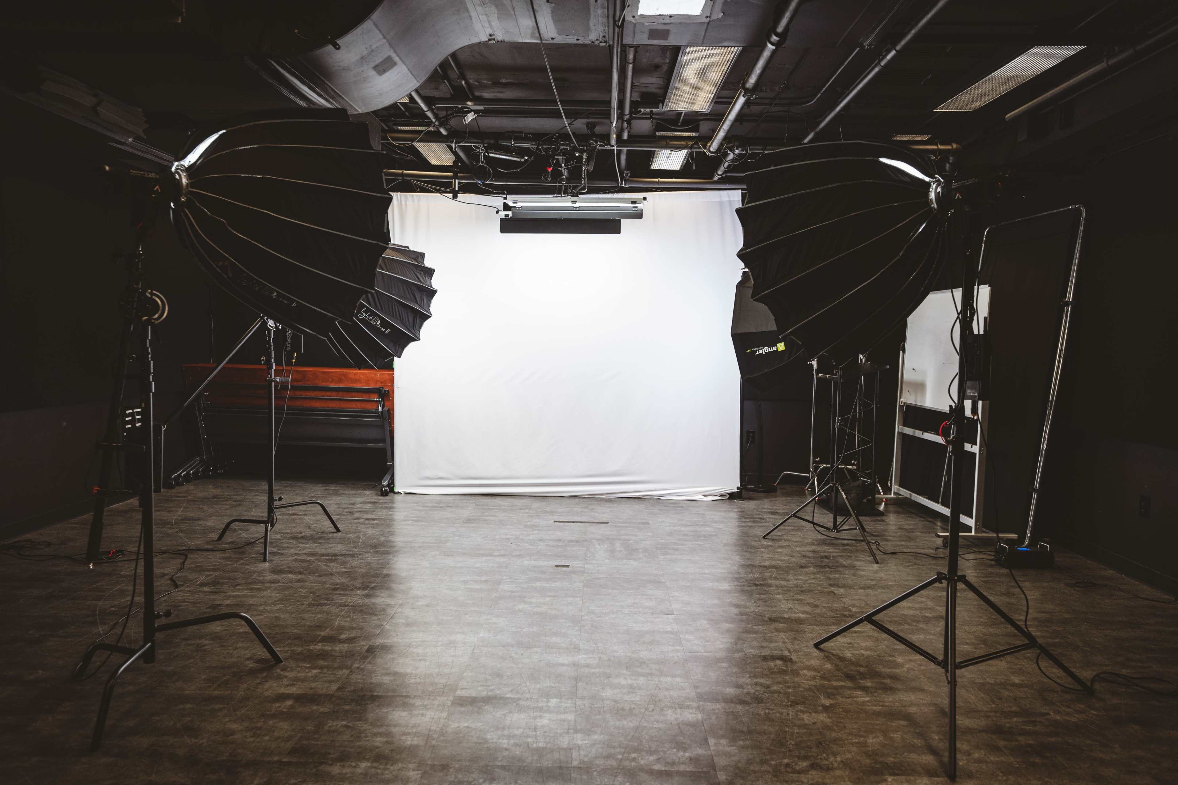 A photography studio features two large softbox lights positioned on either side of a white backdrop.