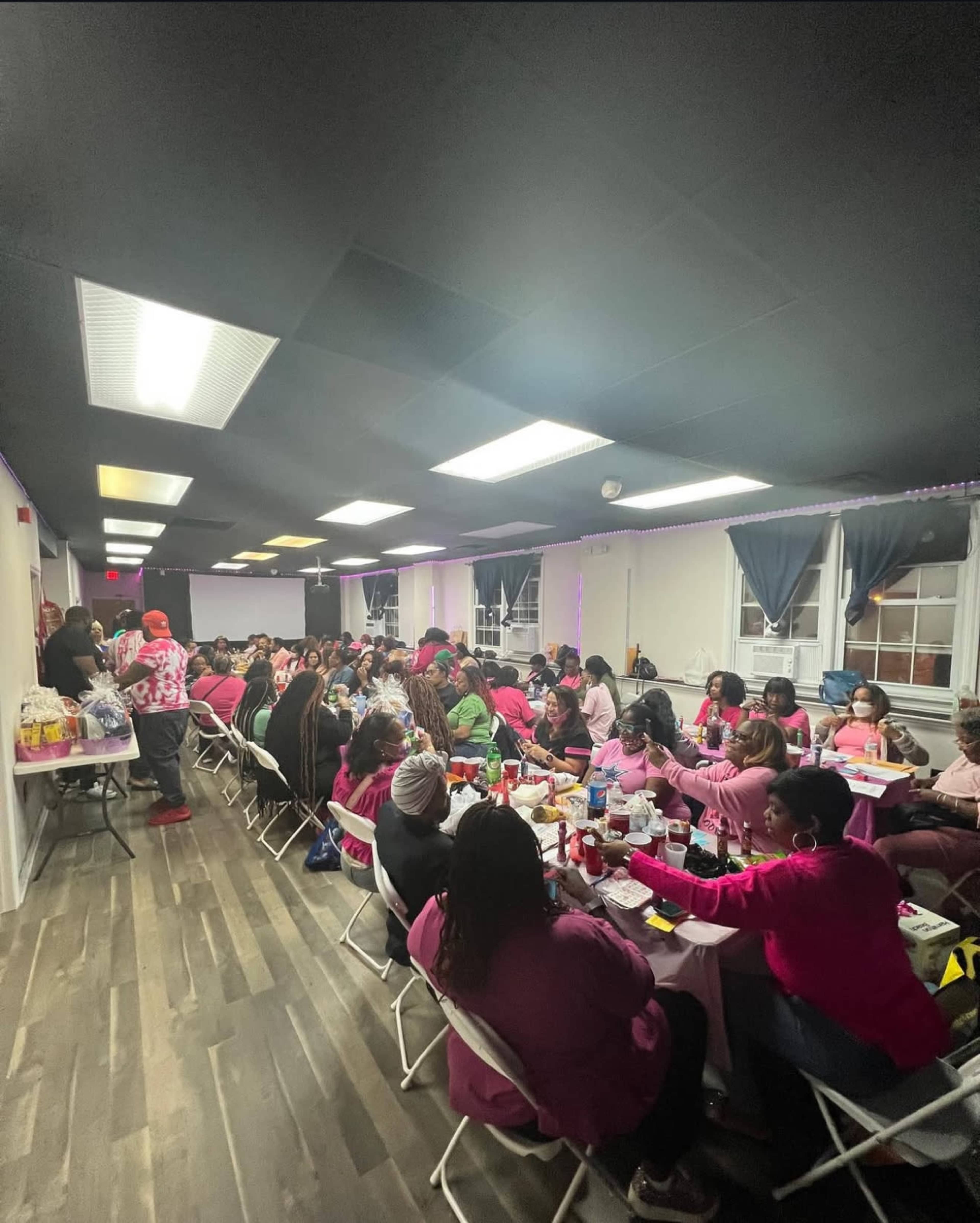 A large group of people dressed in pink is gathered around tables in a brightly lit room, engaged in conversation and activities.