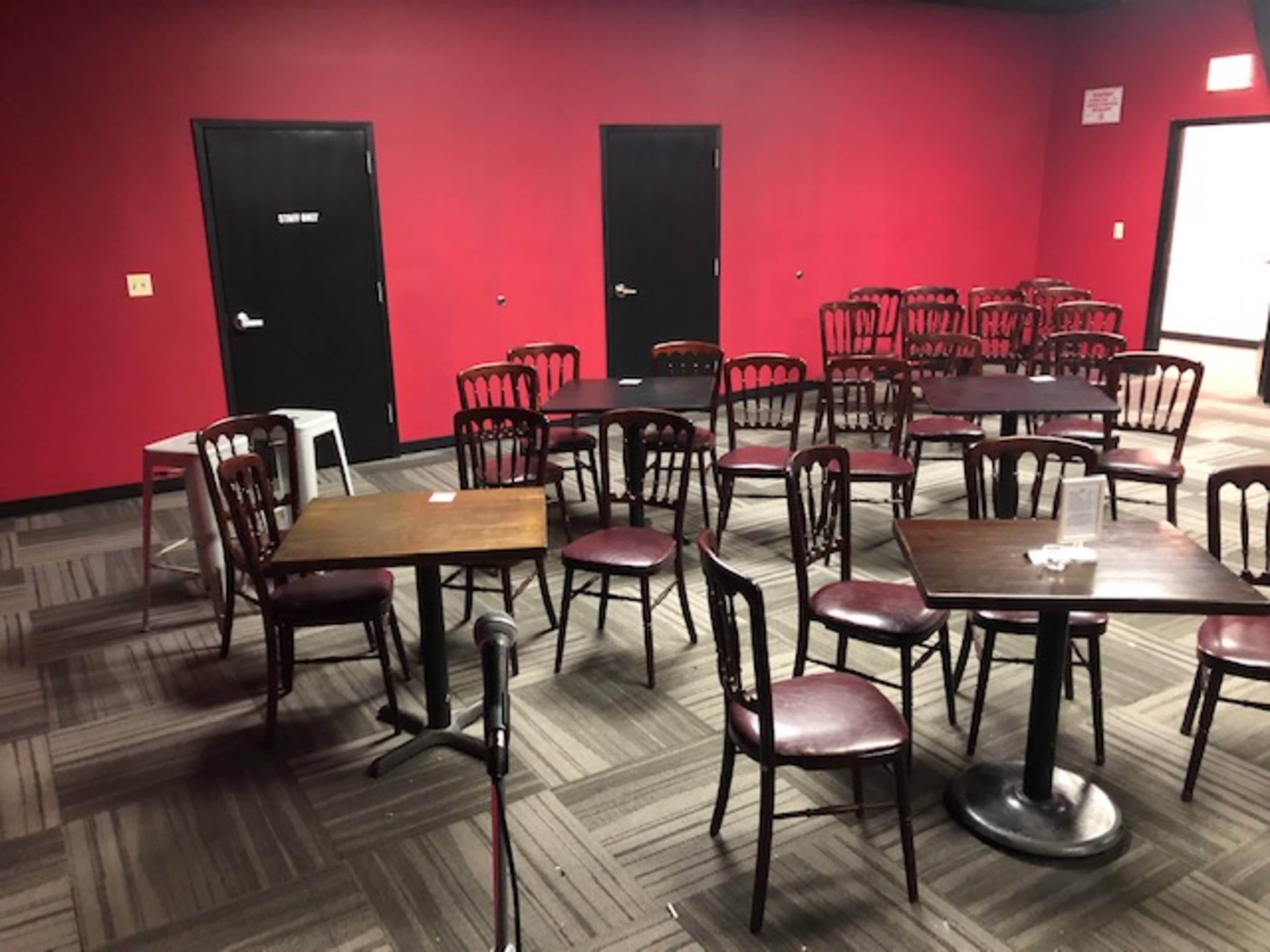 A small room with red walls, several wooden tables and chairs arranged haphazardly, and two closed doors.