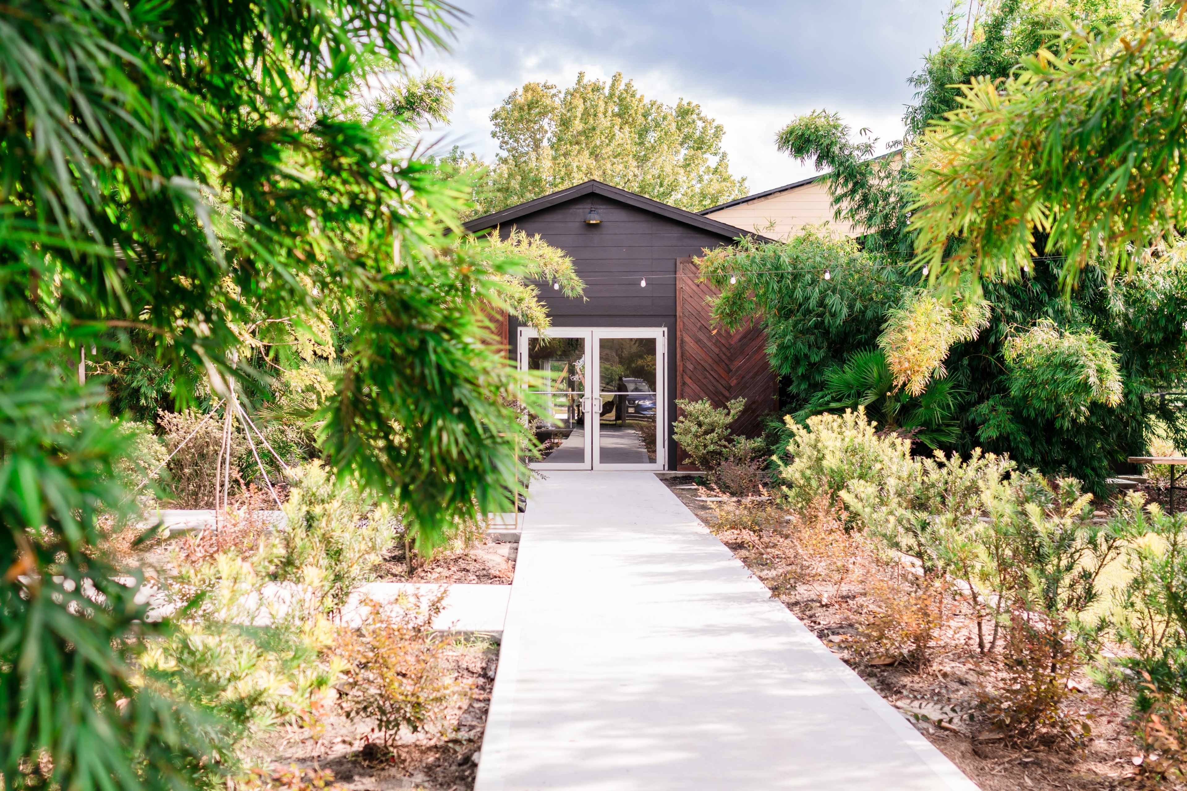 A concrete pathway leads to a modern black building surrounded by lush greenery.