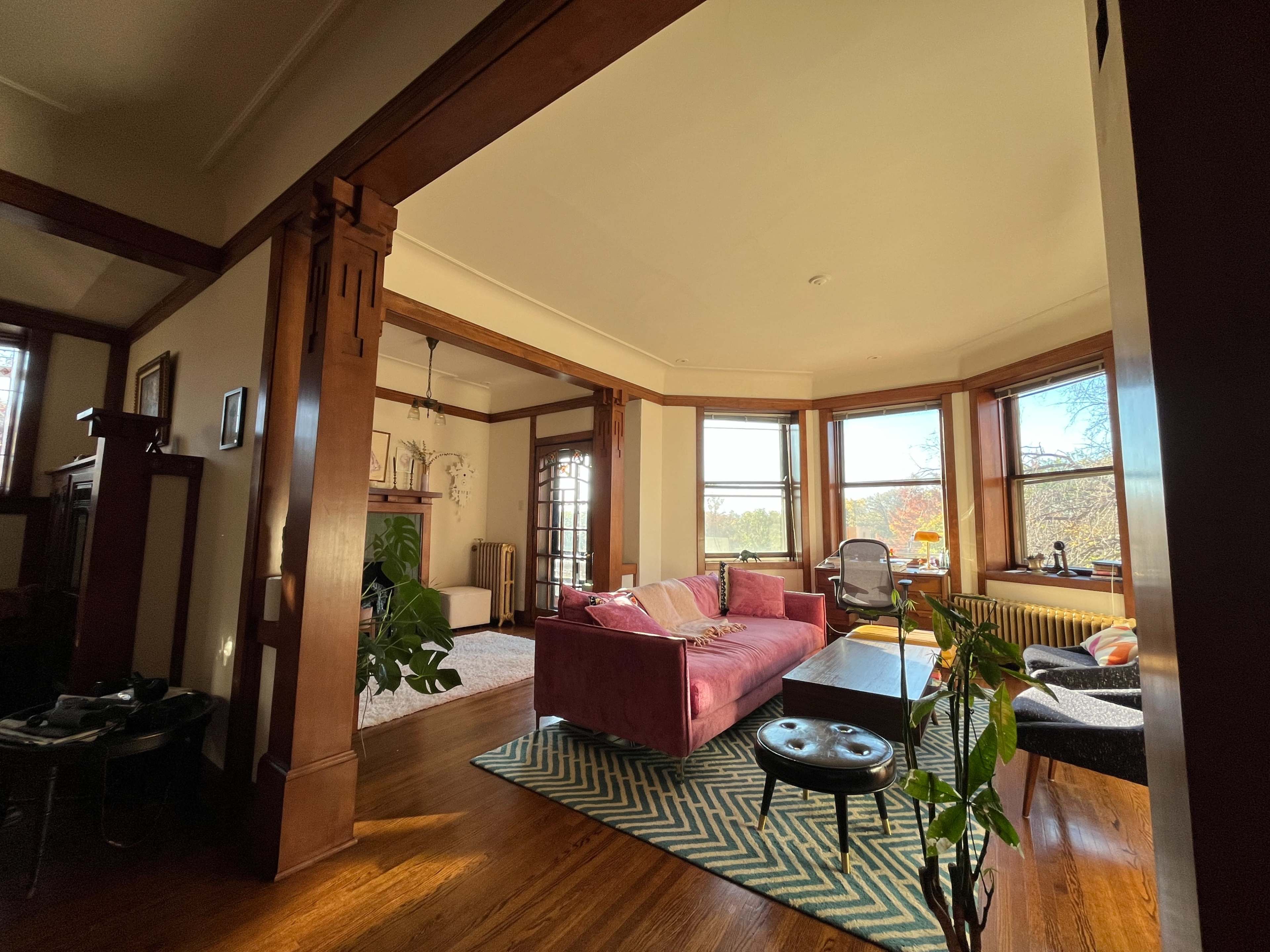 The image shows a spacious living room with a pink sofa, a wooden coffee table, and large windows that provide a view of the outdoors.