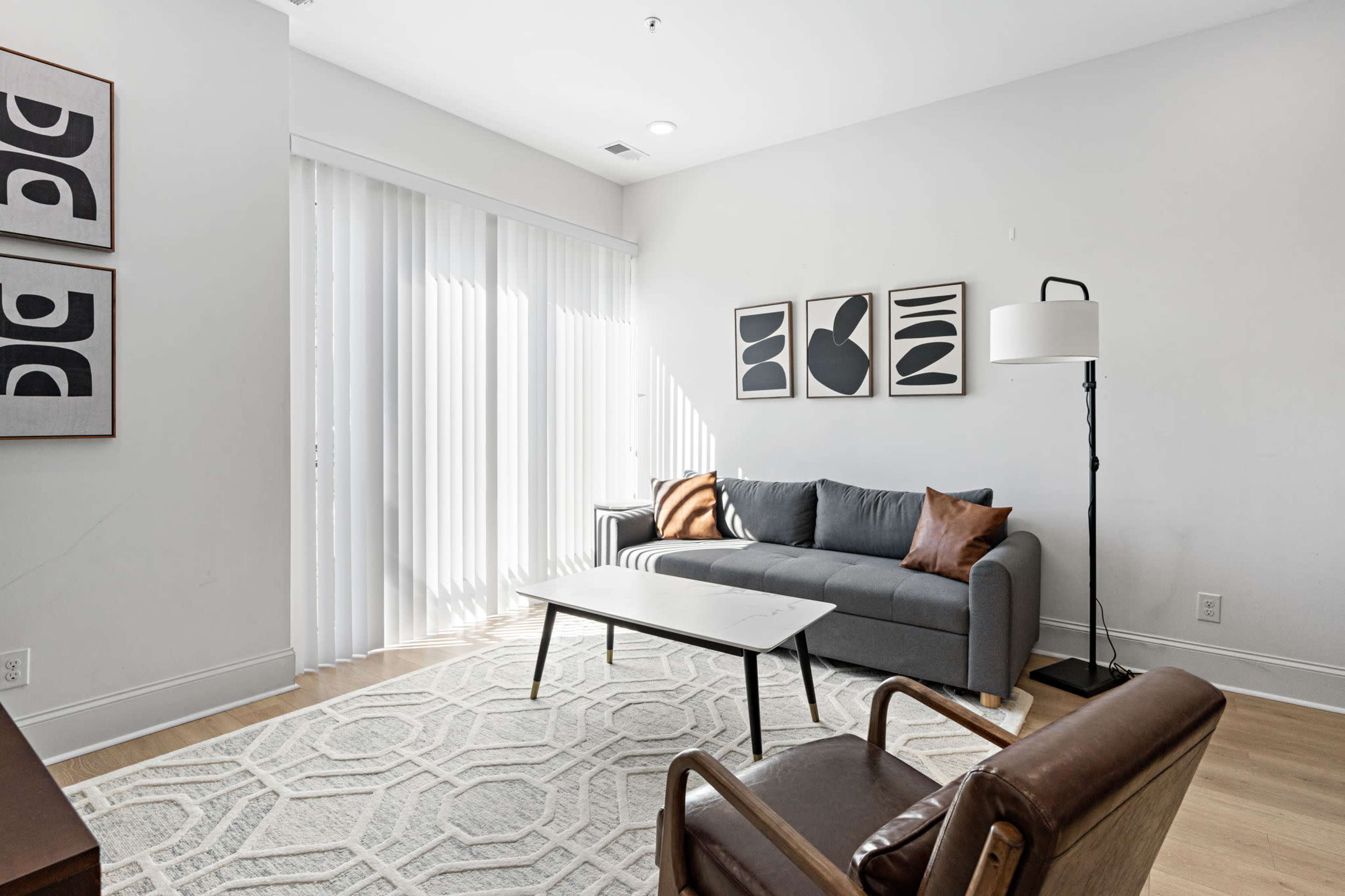 A modern living room with a gray sofa, a coffee table, and a patterned rug, illuminated by natural light from sliding glass doors.