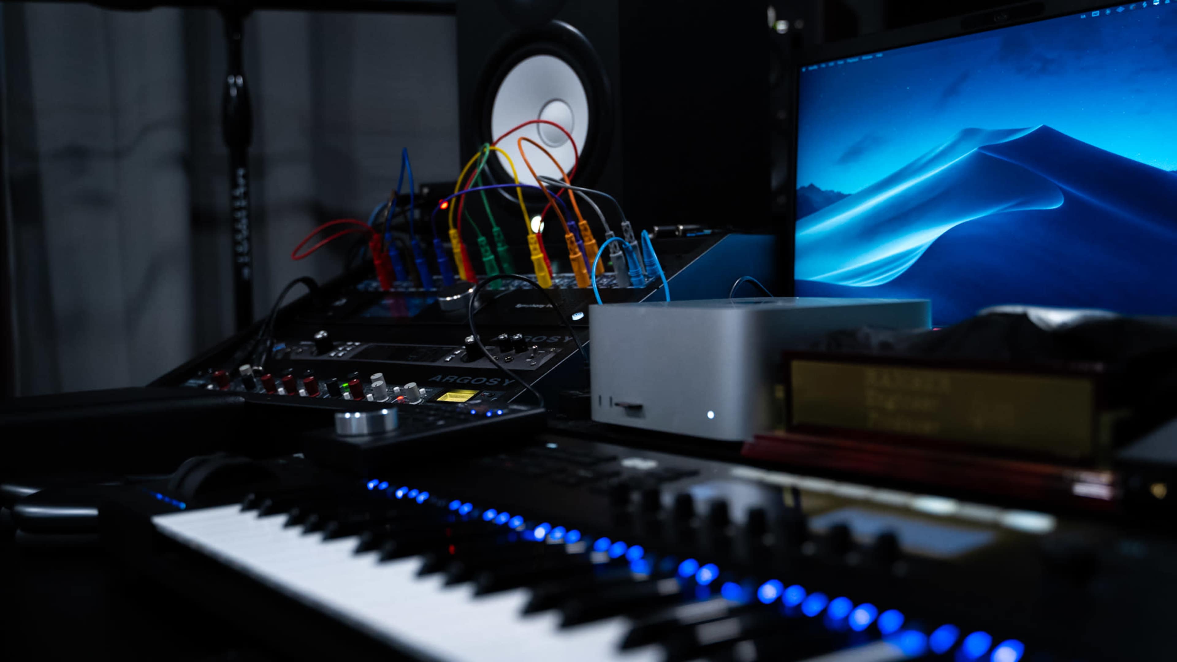 A home music production setup features a keyboard, audio interface, and a computer with colorful cables connected to a modular synthesizer.