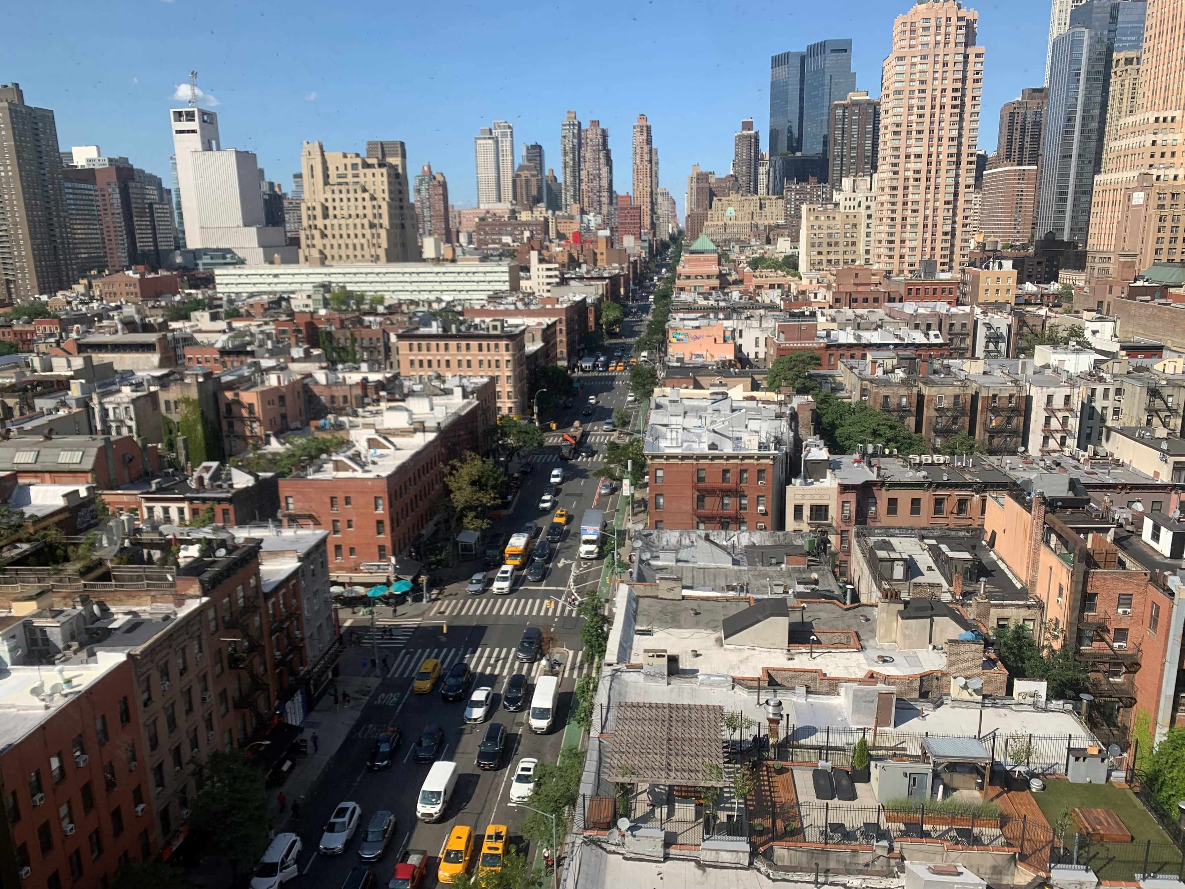 A cityscape of New York, showcasing a mix of tall buildings and lower-rise structures along a busy street filled with vehicles.
