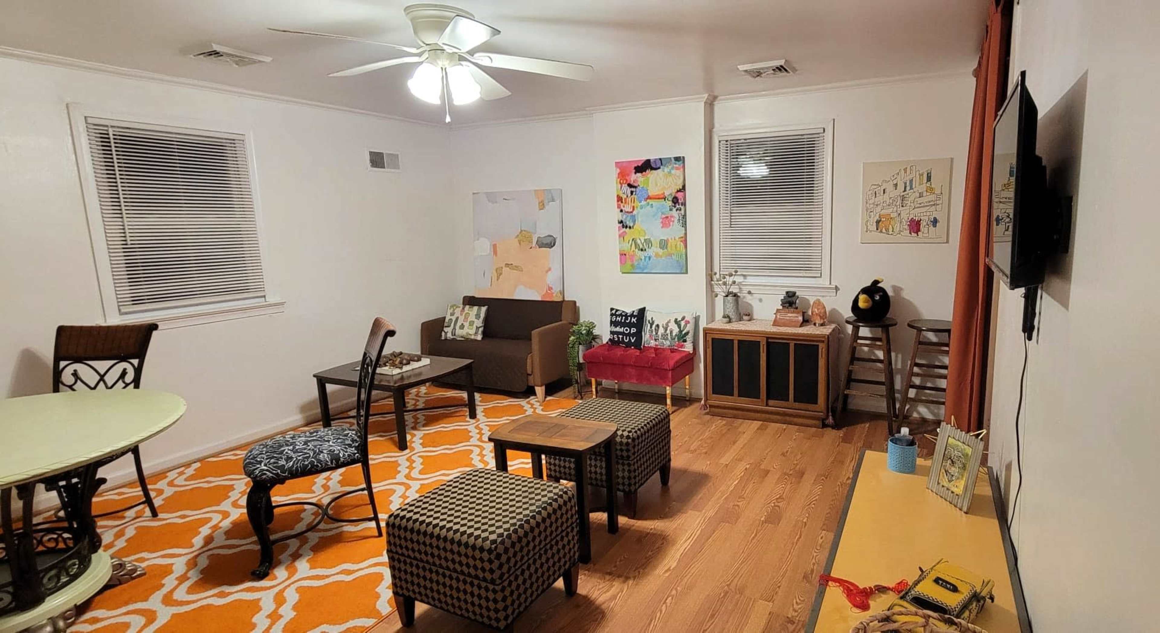 A living room with a circular dining table, several chairs, a couch, a coffee table, and walls adorned with various artworks.