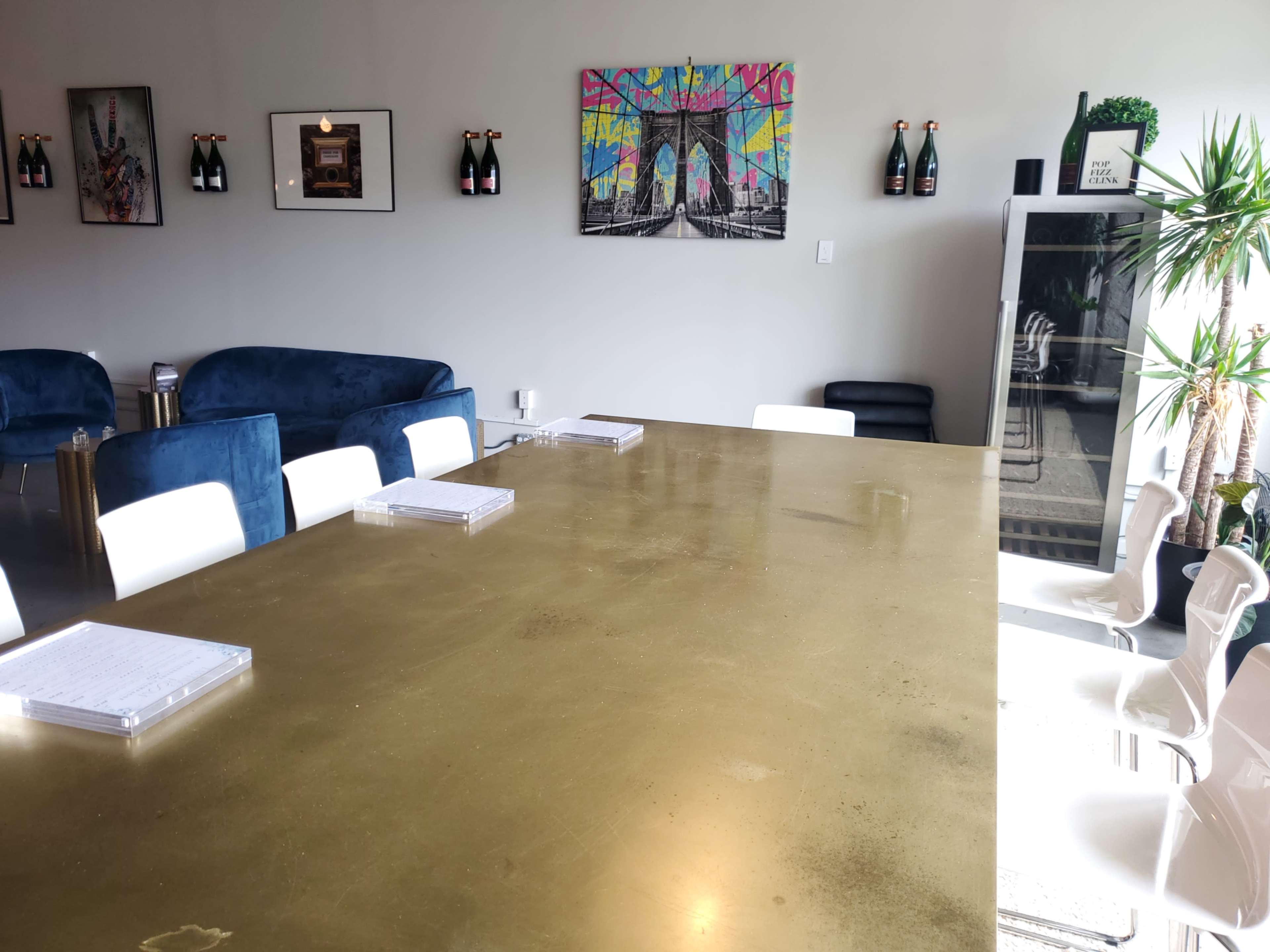 A large, shiny gold table is centered in a modern room with white chairs, and various artworks and decorations on the walls.