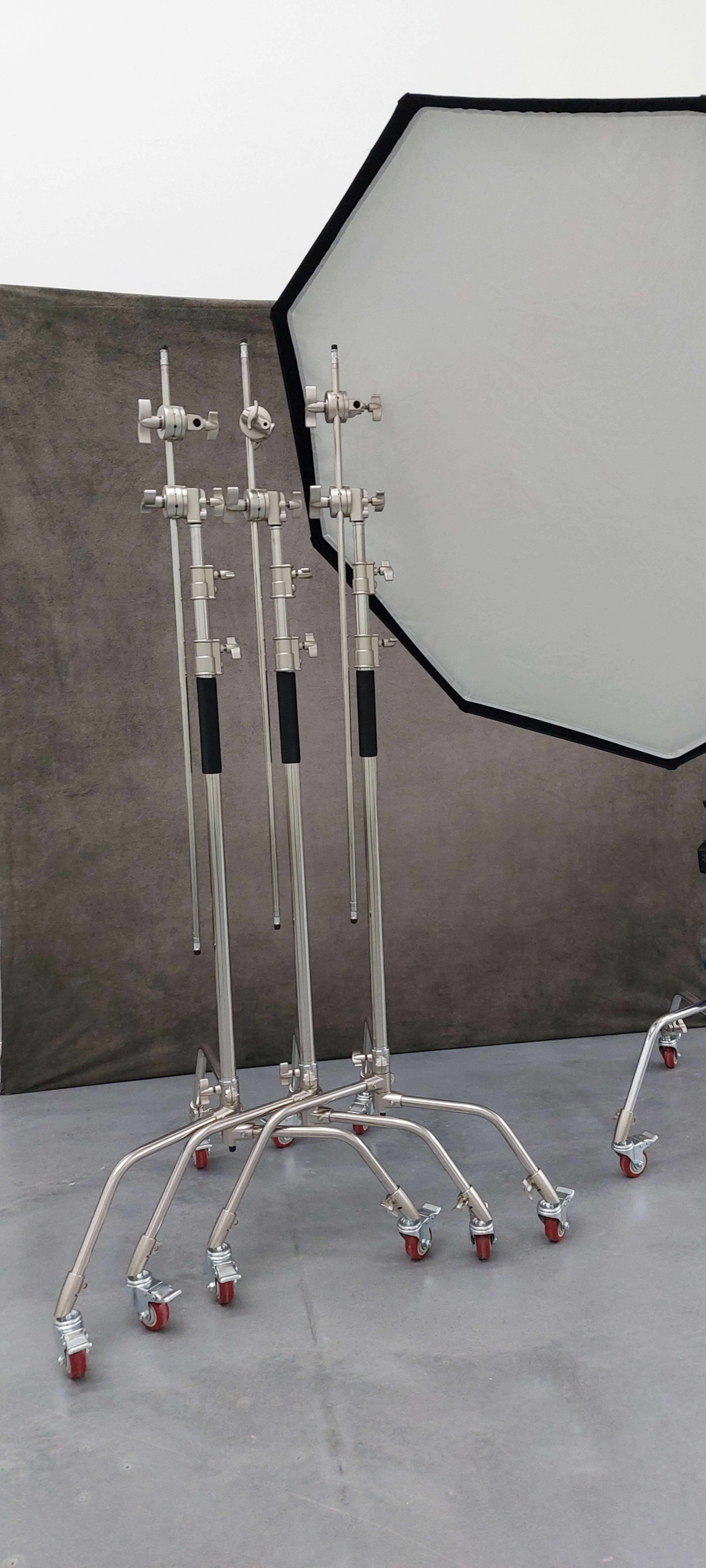 The image features several silver light stands with wheels and a large softbox positioned to the right on a gray floor.