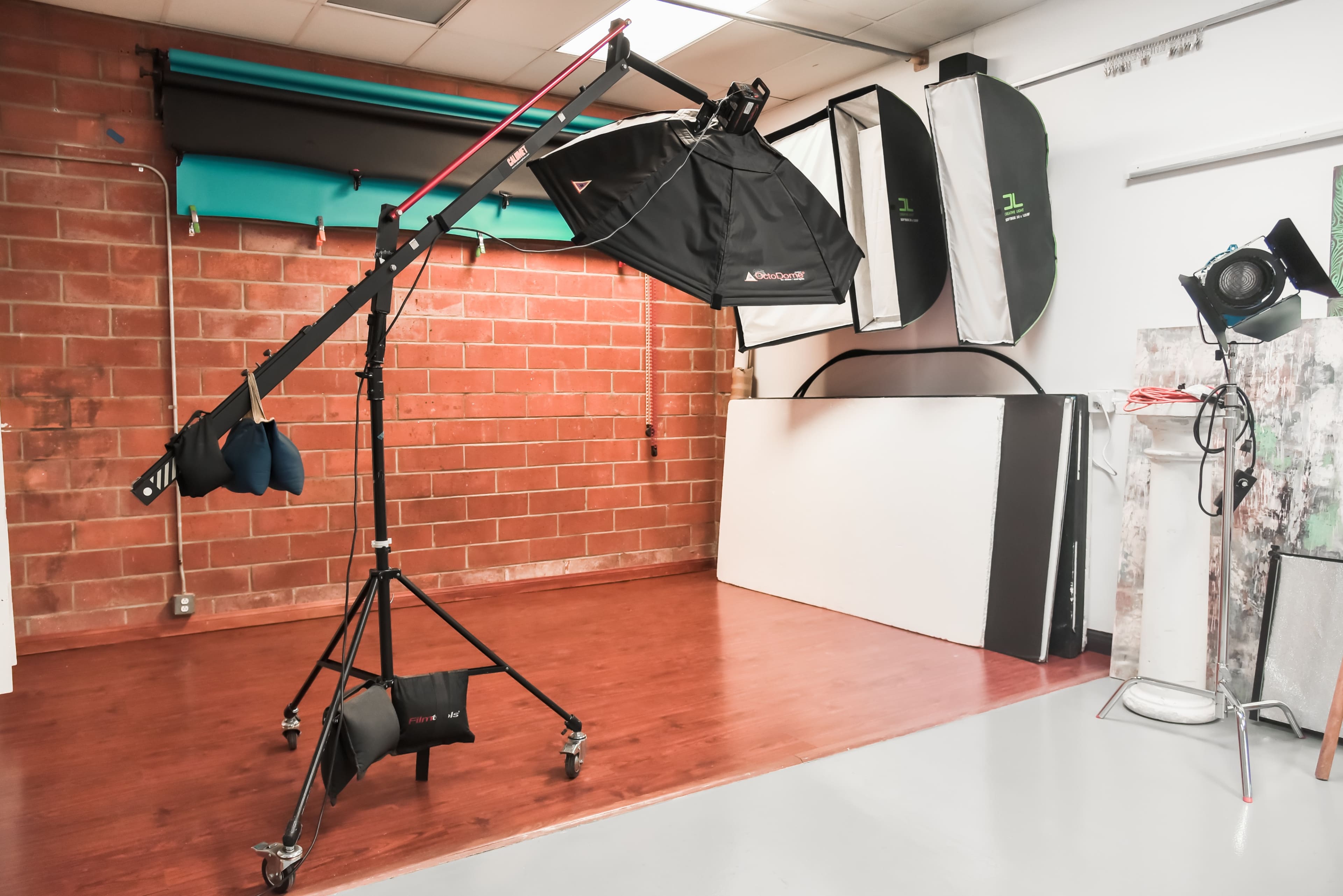 A photography studio setup with a light stand equipped with a softbox, a backdrop, and various photography equipment arranged against a brick wall.