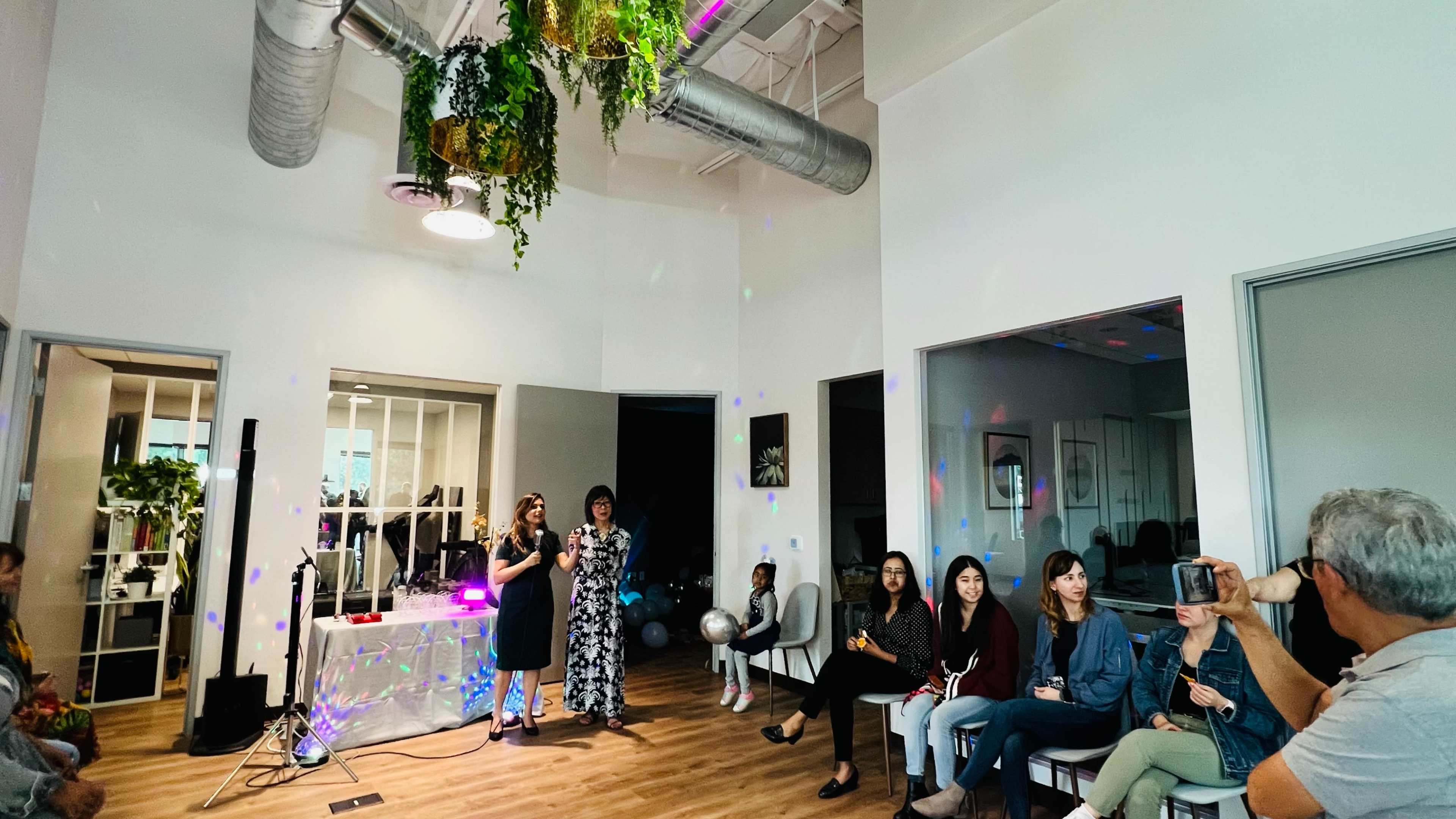 A group of people gathers in a brightly lit room with colorful lighting effects and a table with refreshments.
