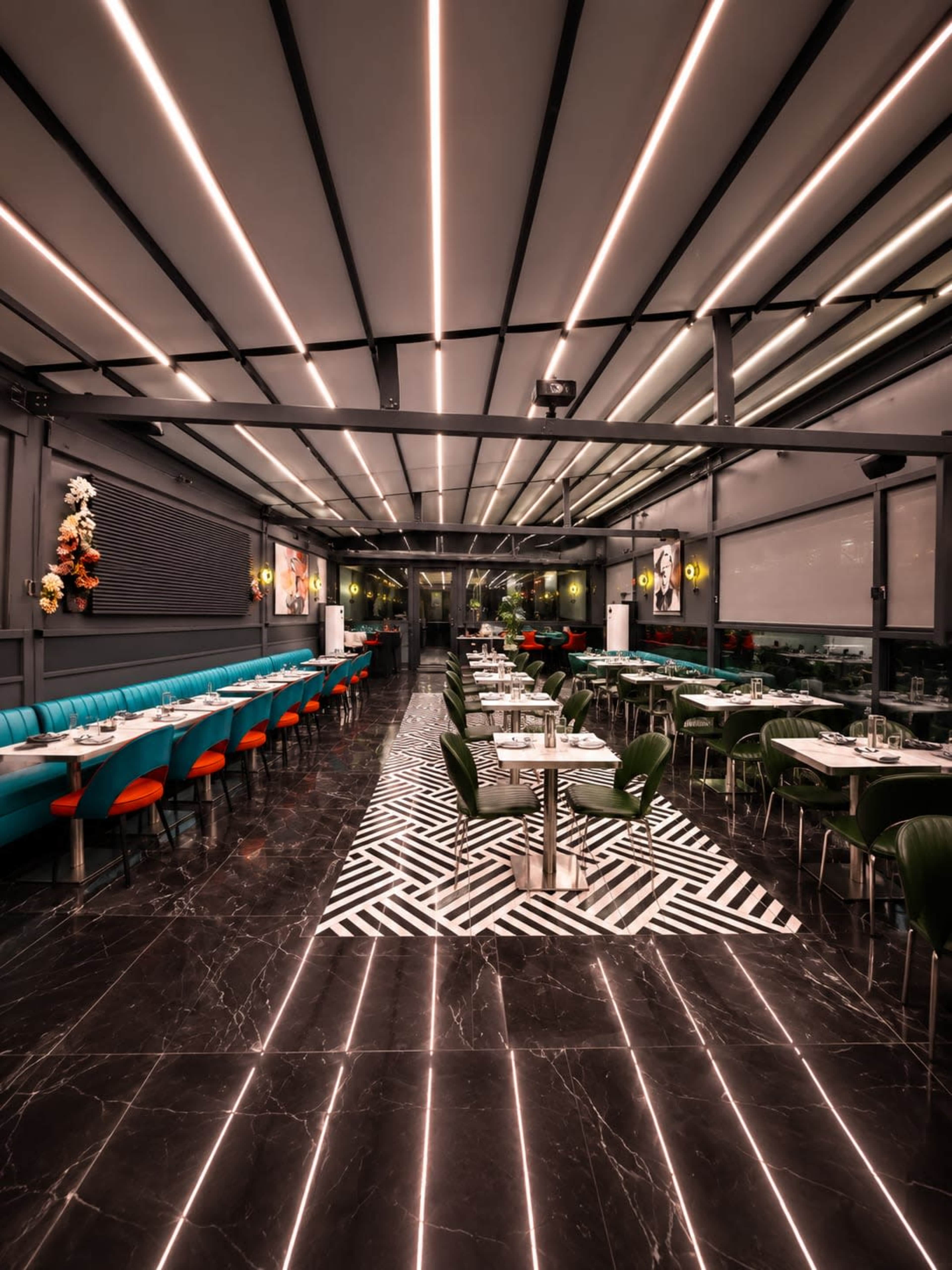 The image shows a modern restaurant interior featuring a sleek design with green and red seating, a patterned black and white floor, and linear ceiling lighting.