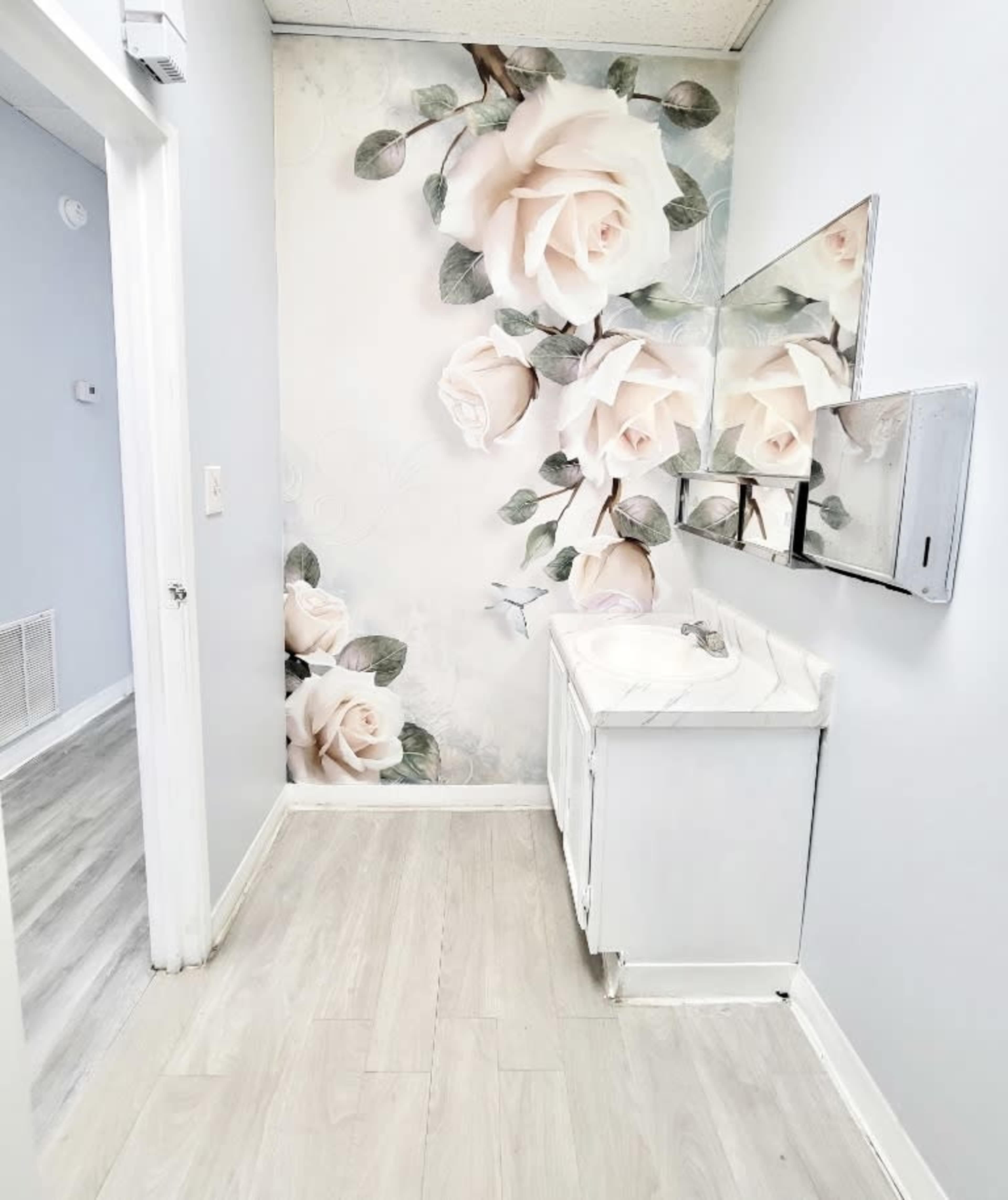 A bathroom with a floral mural of large white roses on one wall, featuring a small sink with a mirror above it.