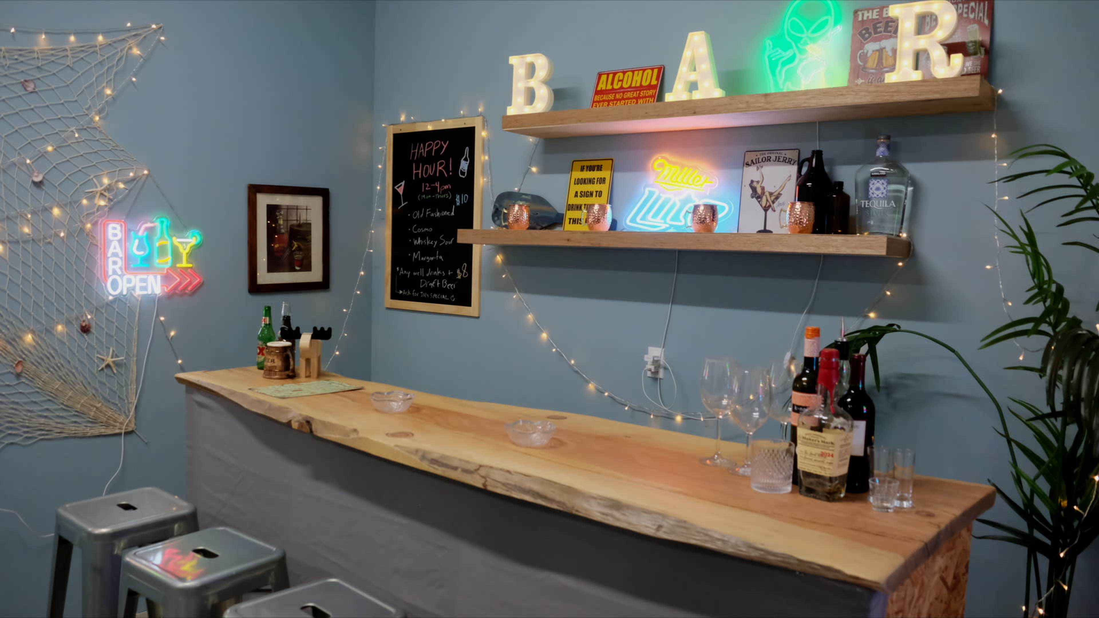 The image shows a small home bar area with a wooden counter, shelves displaying various bottles and decorations, and twinkling lights.
