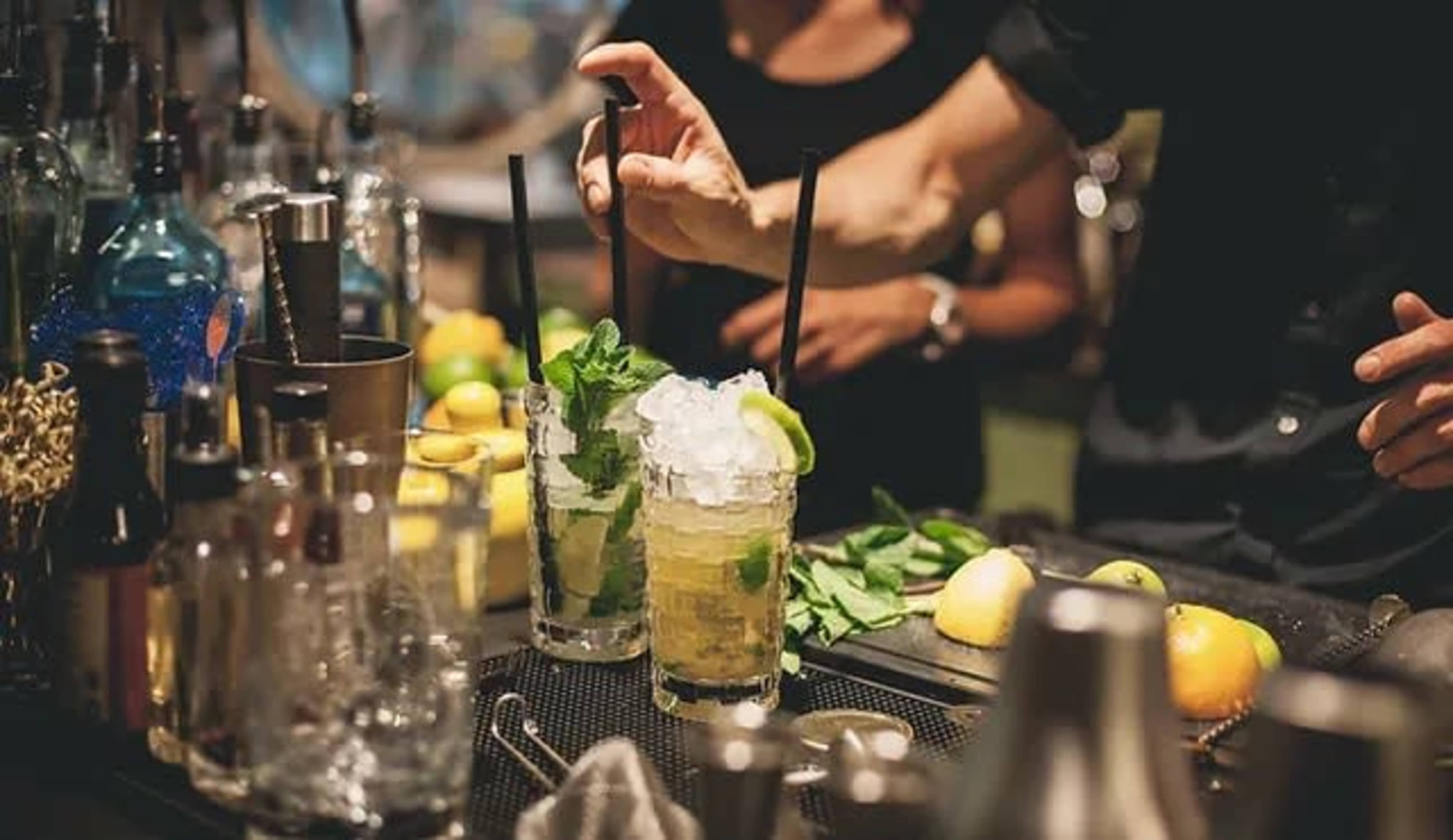 A bartender prepares cocktails with fresh mint and ice at a bar.