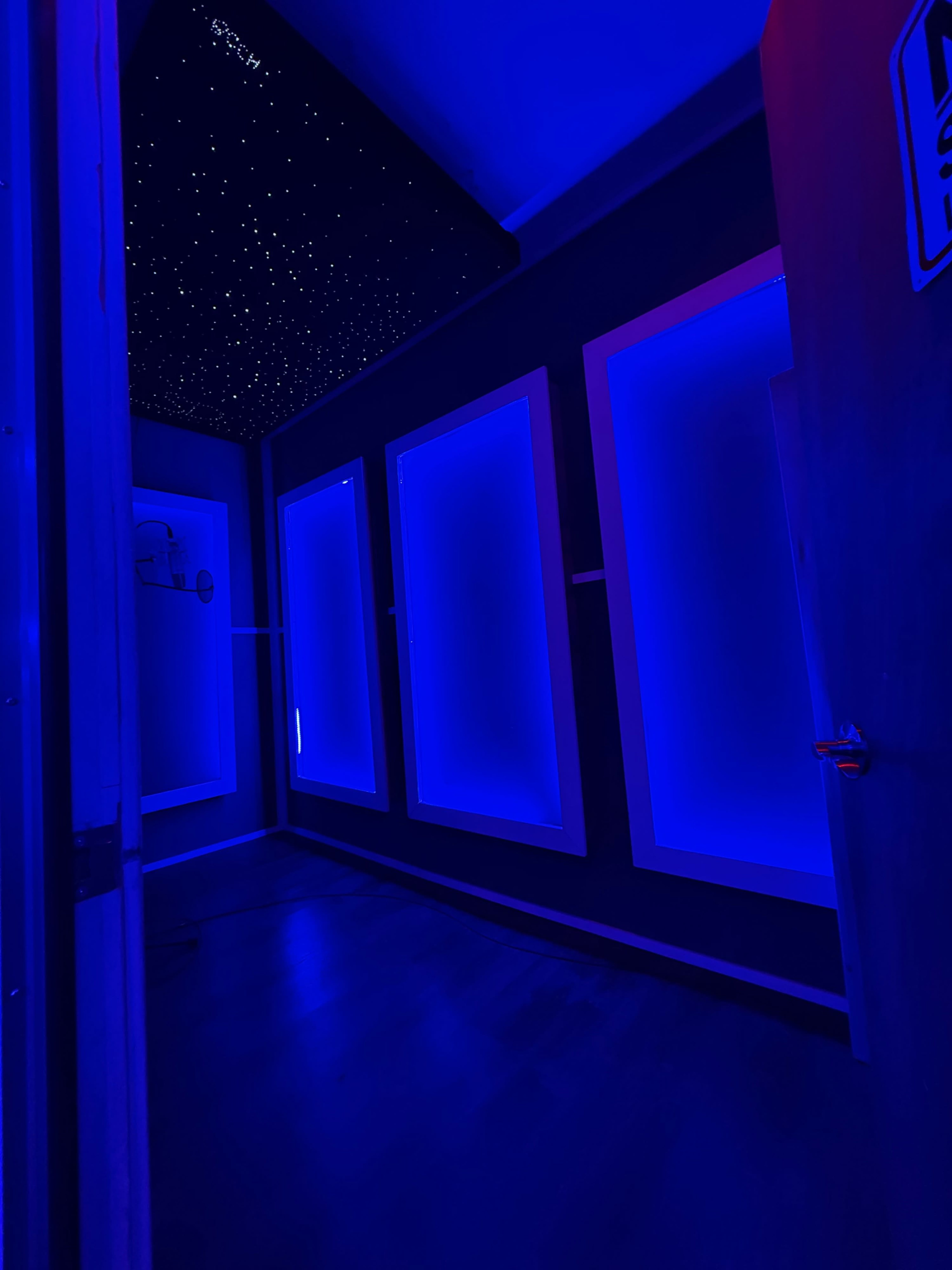 The image shows a dimly lit room with blue LED lighting, featuring four illuminated panels on the walls and a ceiling resembling a starry night sky.