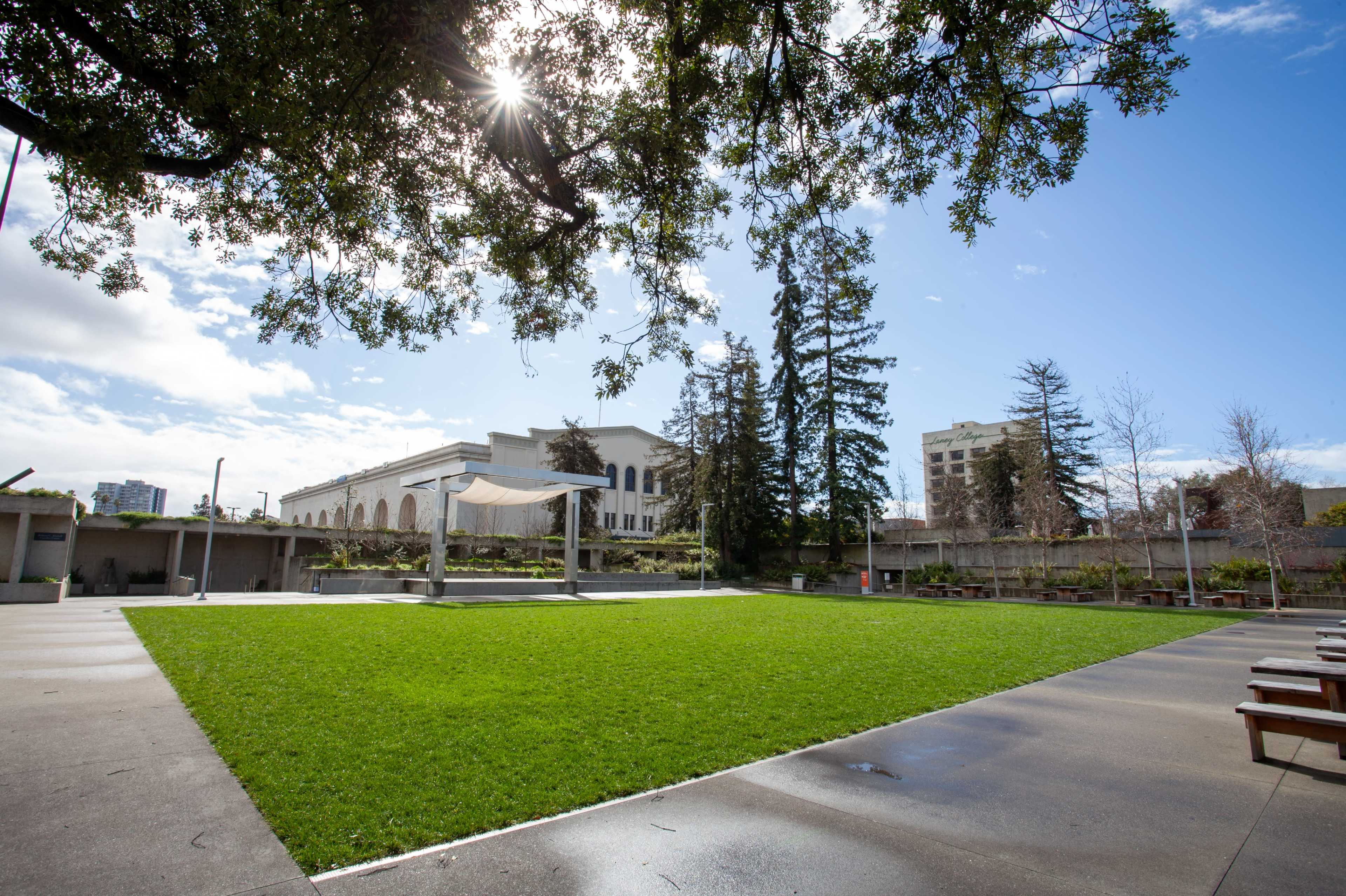A large grassy area is framed by trees and buildings under a partly cloudy sky.