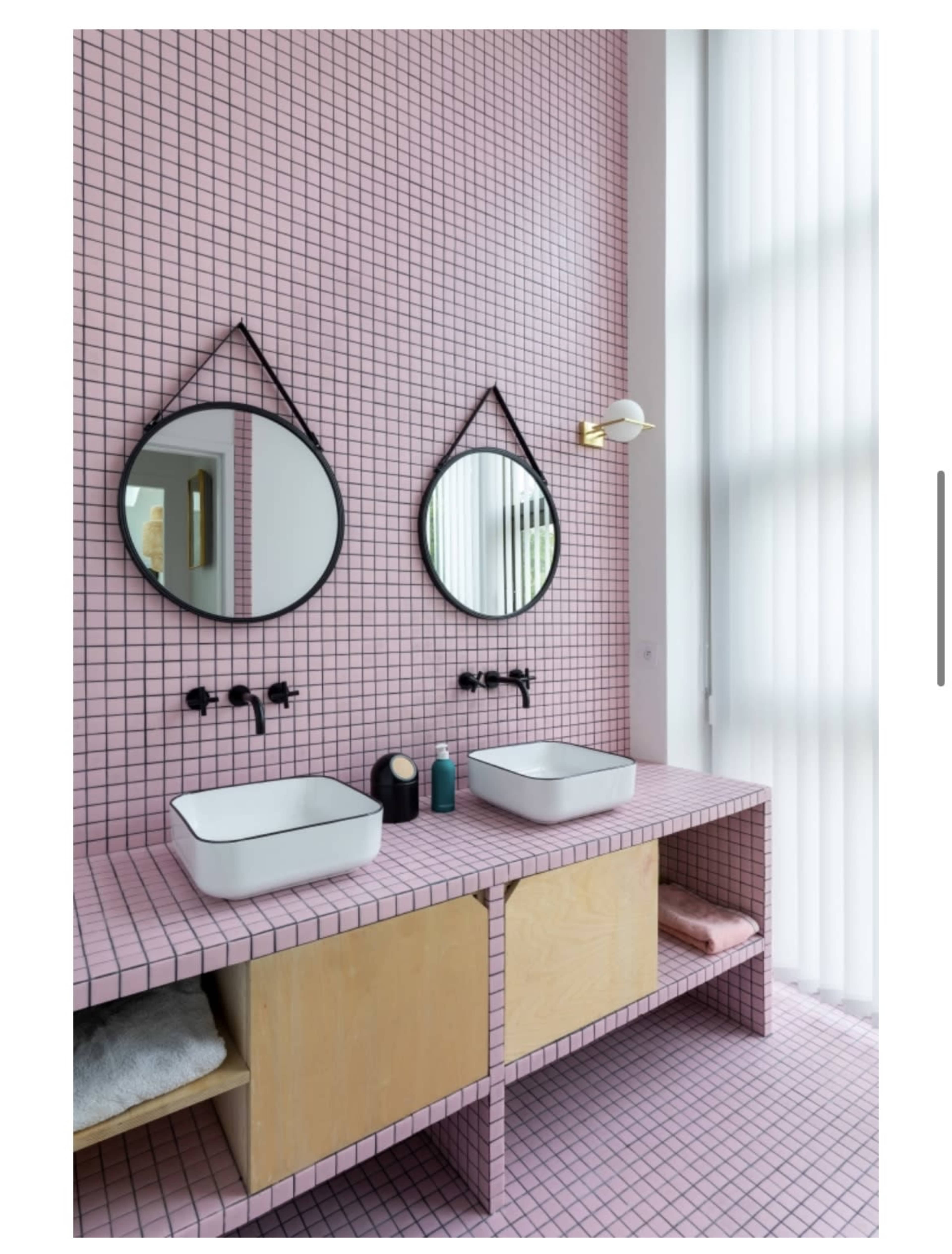 A bathroom with pink tiled walls, two round mirrors, and a wooden vanity featuring two modern sinks.