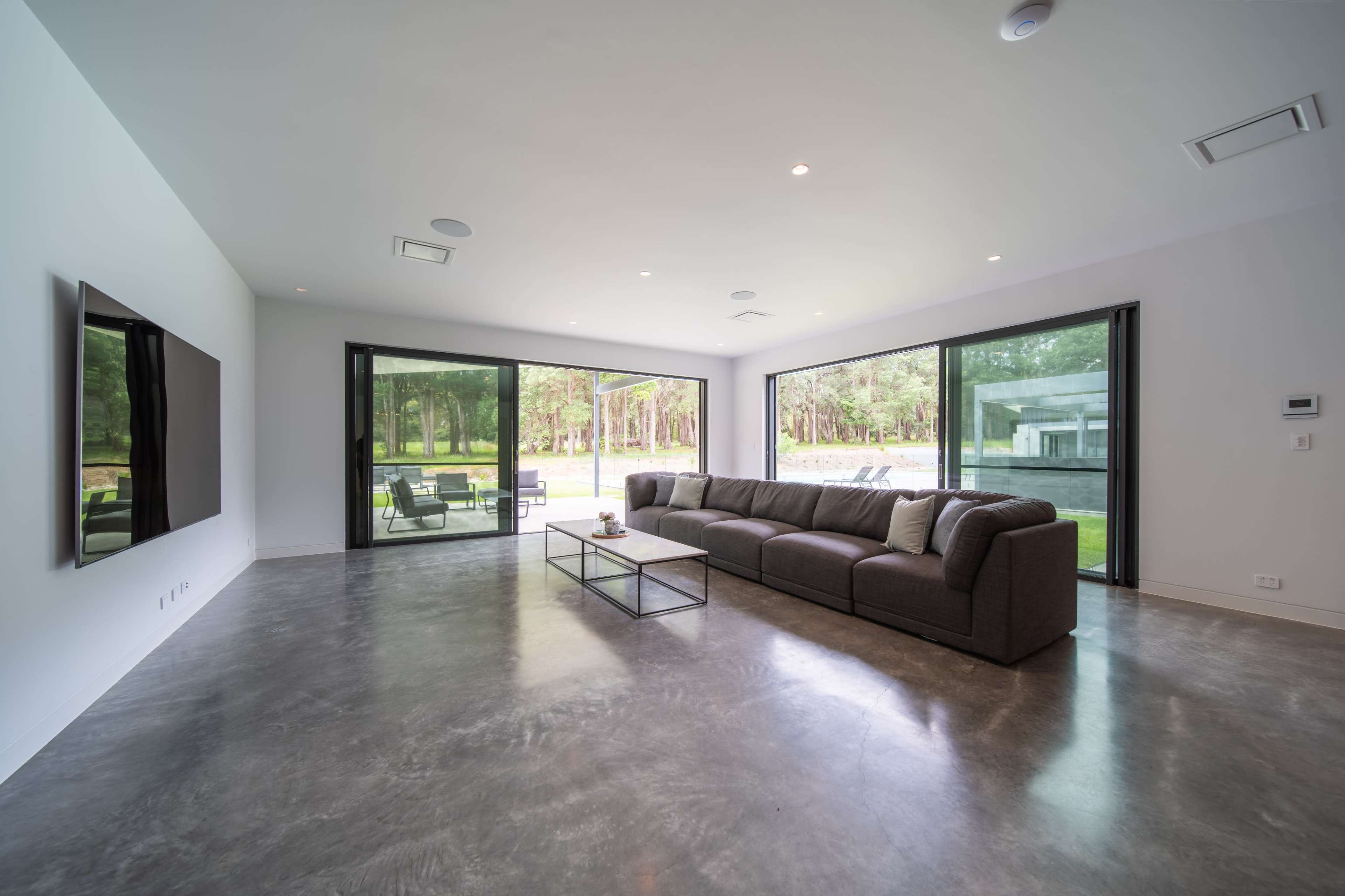 A modern living room with a large gray sofa, a glass coffee table, and expansive windows that provide a view of a lush outdoor setting.