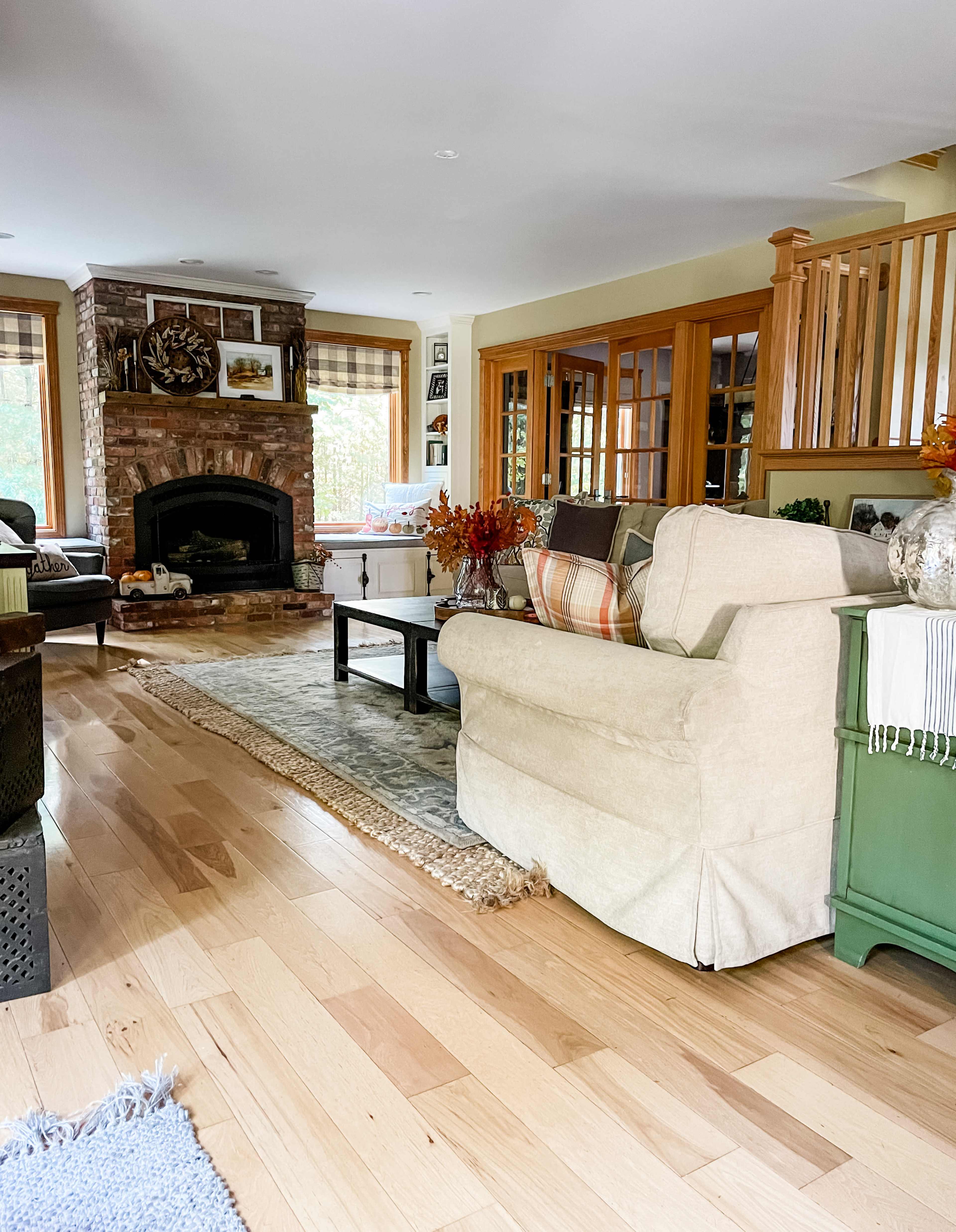The living room features a stone fireplace, a mix of comfortable seating, and wooden decor elements, all set against a backdrop of large windows and hardwood flooring.