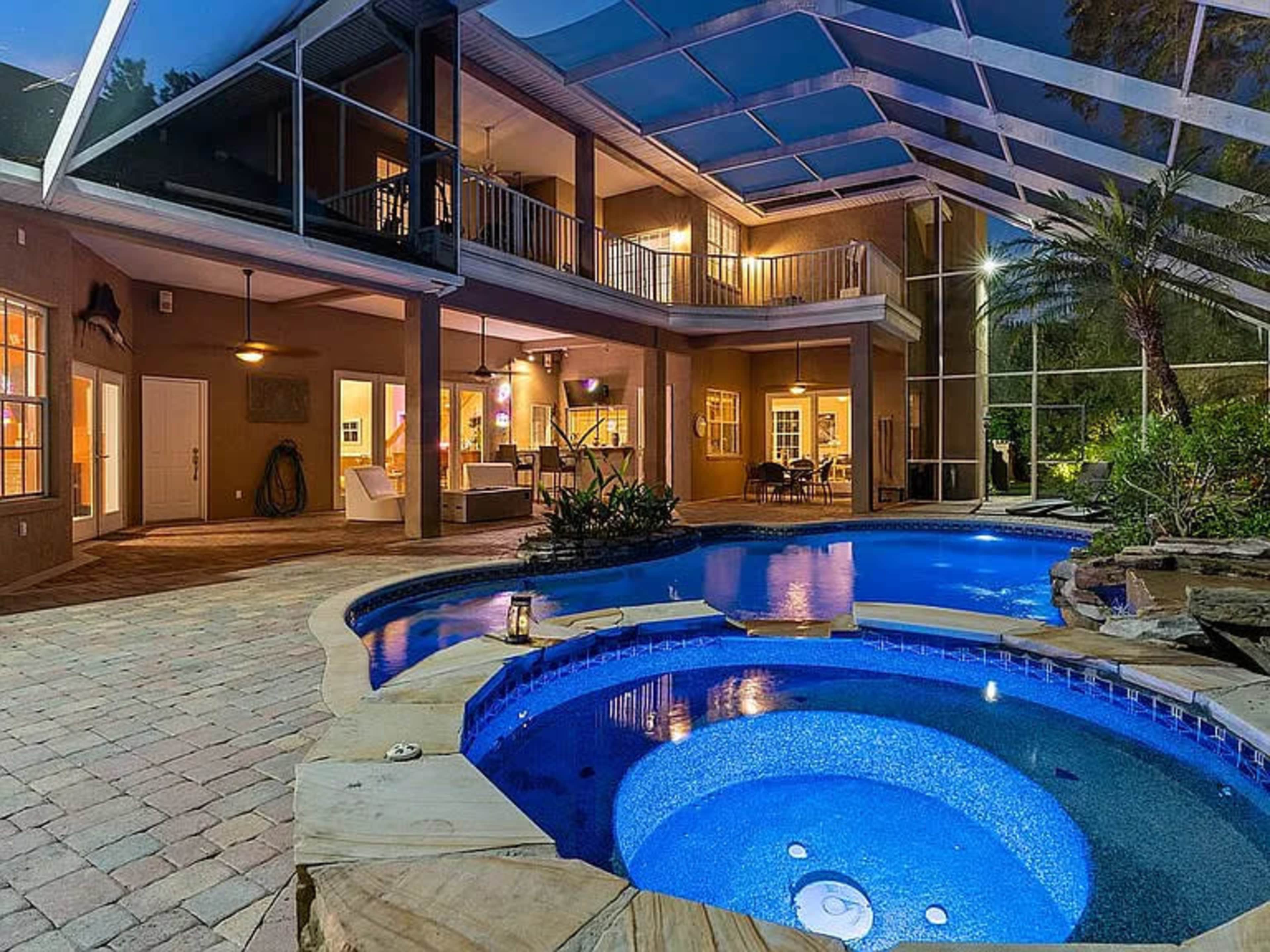 The image shows a spacious backyard with a swimming pool, jacuzzi, and a screened patio area featuring multiple entry points to the house.