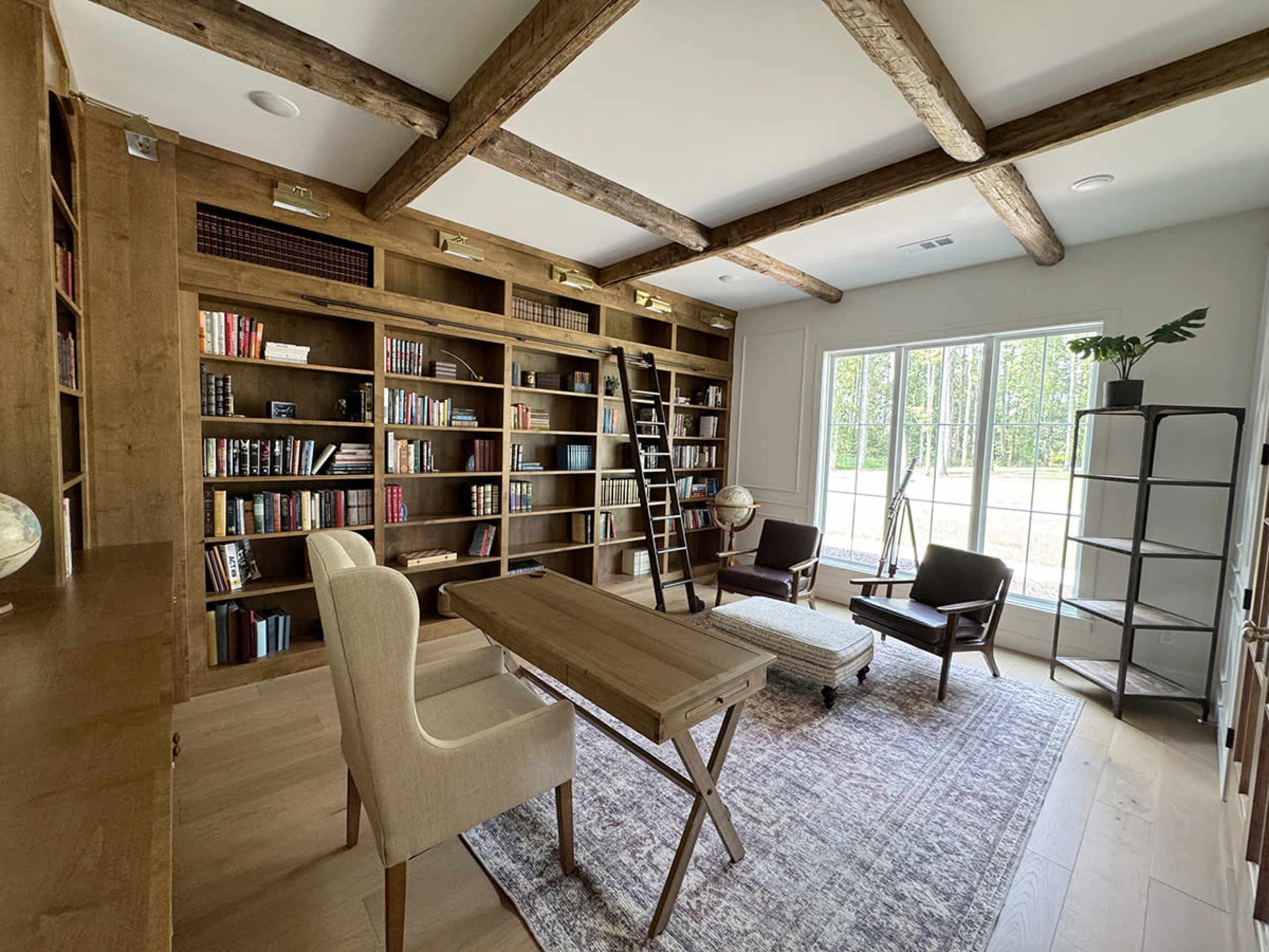 The image shows a modern home office with built-in bookshelves, a wooden table, and a reading area with chairs and a globe.