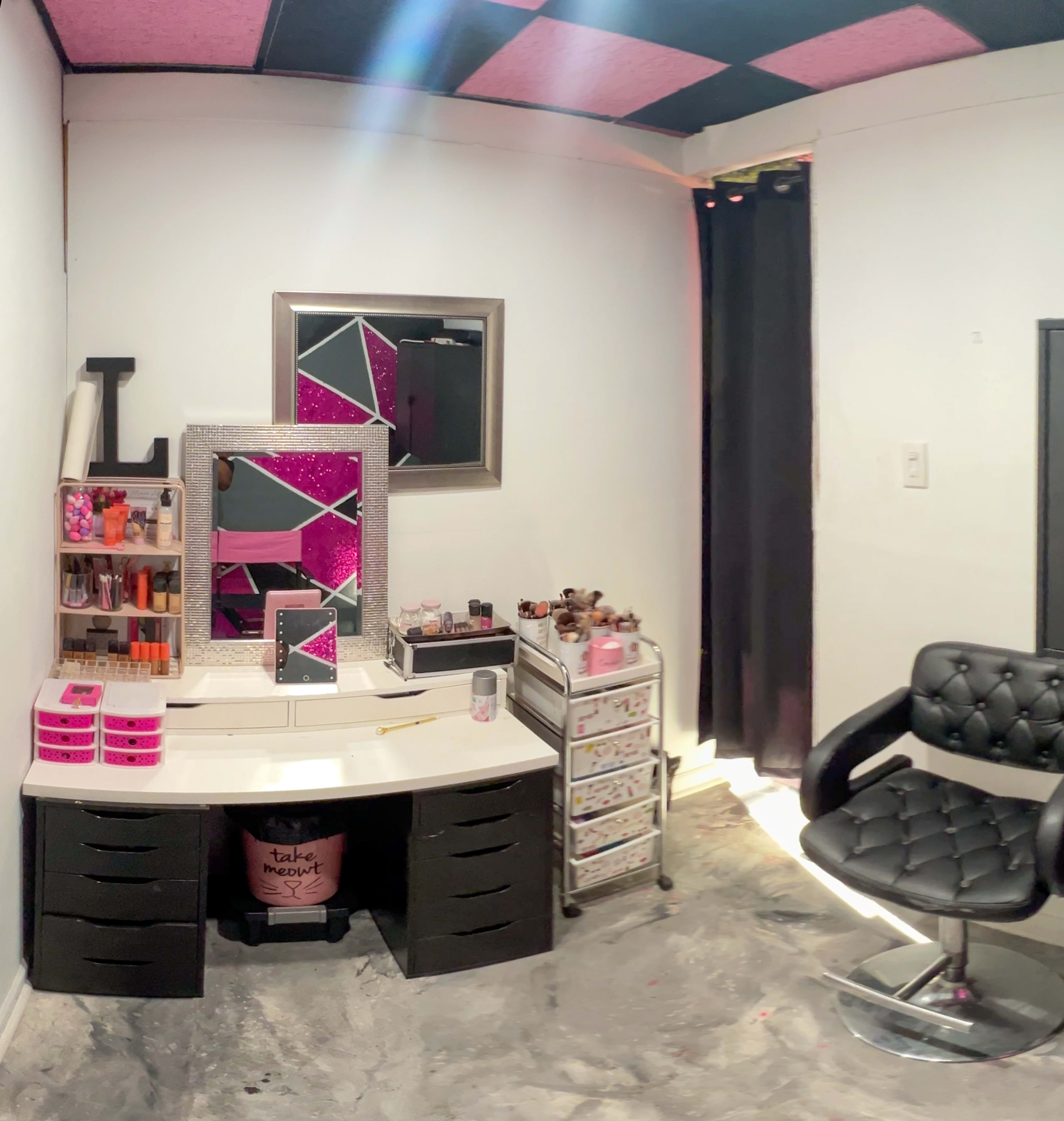 A makeup vanity area with a white desk, a chair, a mirror, and organized makeup products displayed on shelves and drawers.