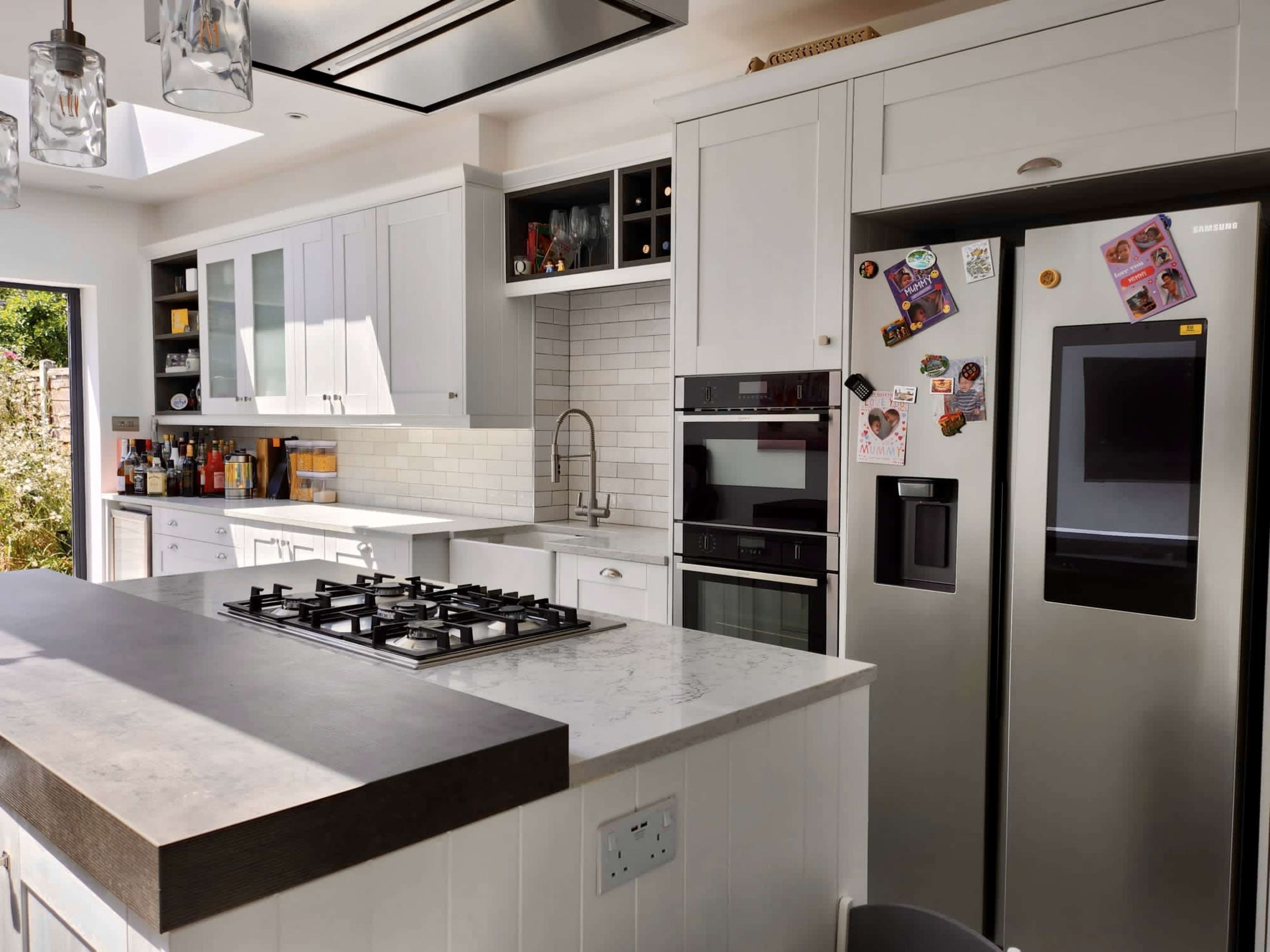The image shows a modern kitchen featuring white cabinets, a large island with a gas cooktop, built-in appliances, and a combination of open and closed shelving.