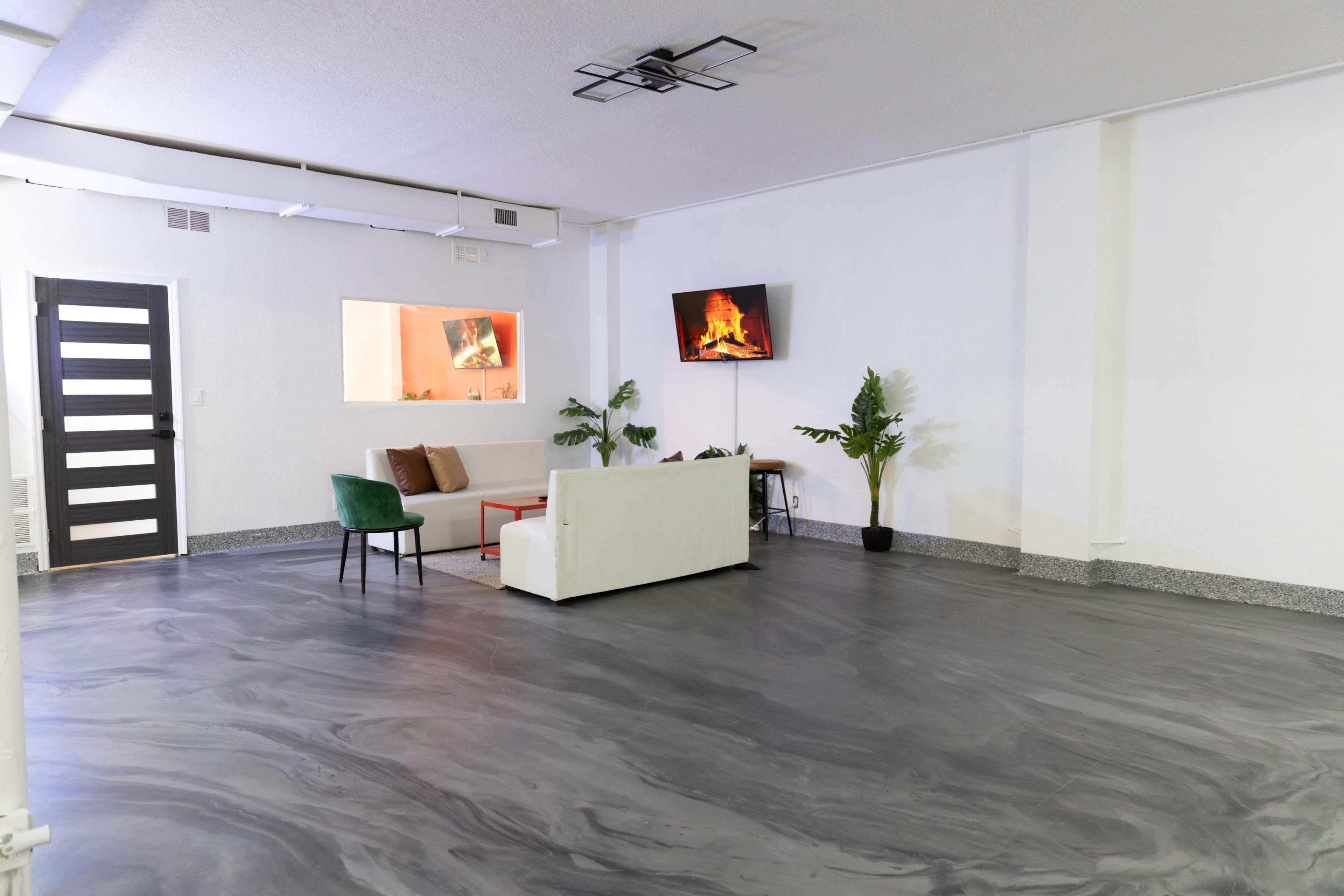 A modern, open space featuring a white couch, two chairs, a wall-mounted television displaying a fireplace, and a small plant.