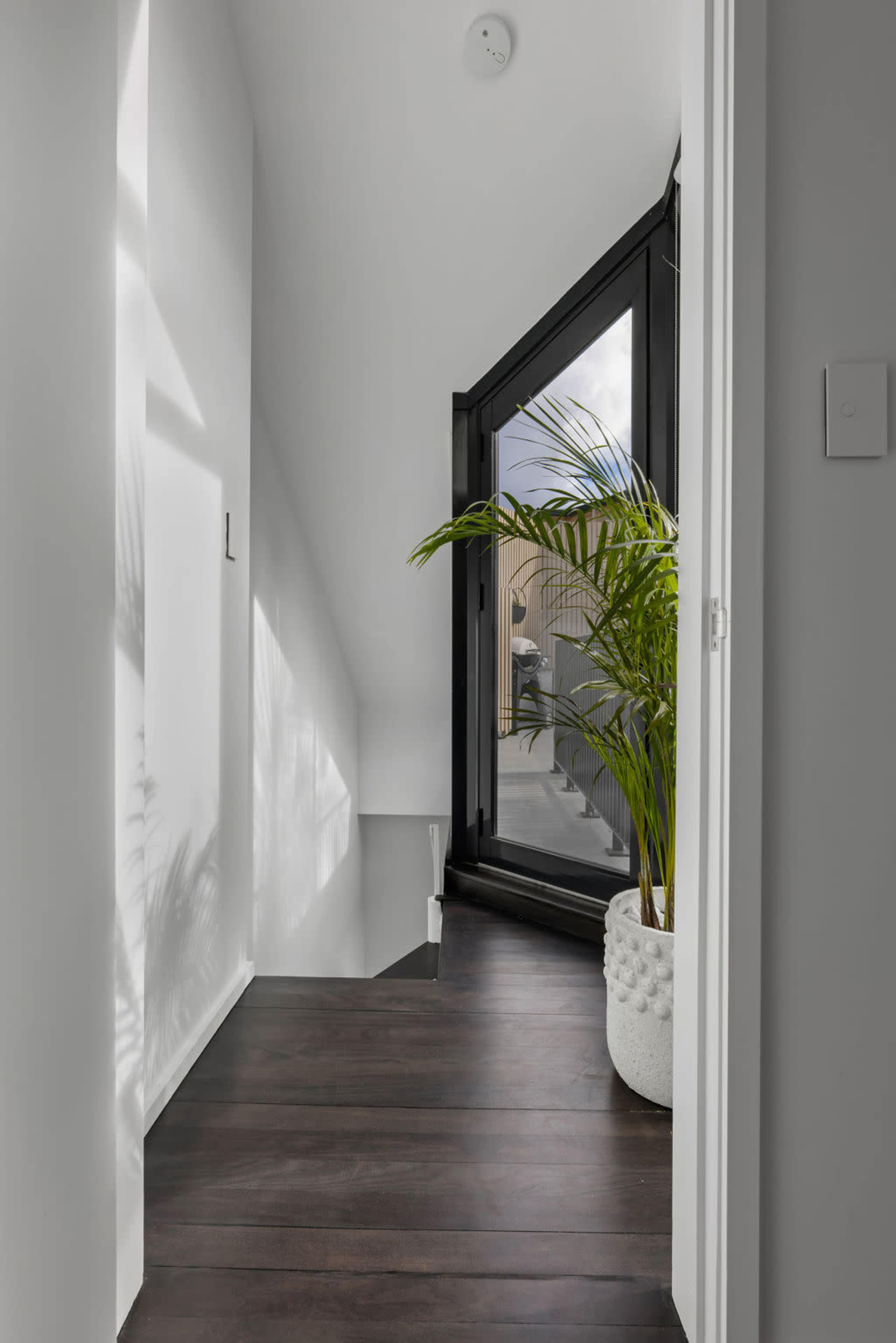 A hallway featuring a large window with a view of a potted plant and light wood flooring.