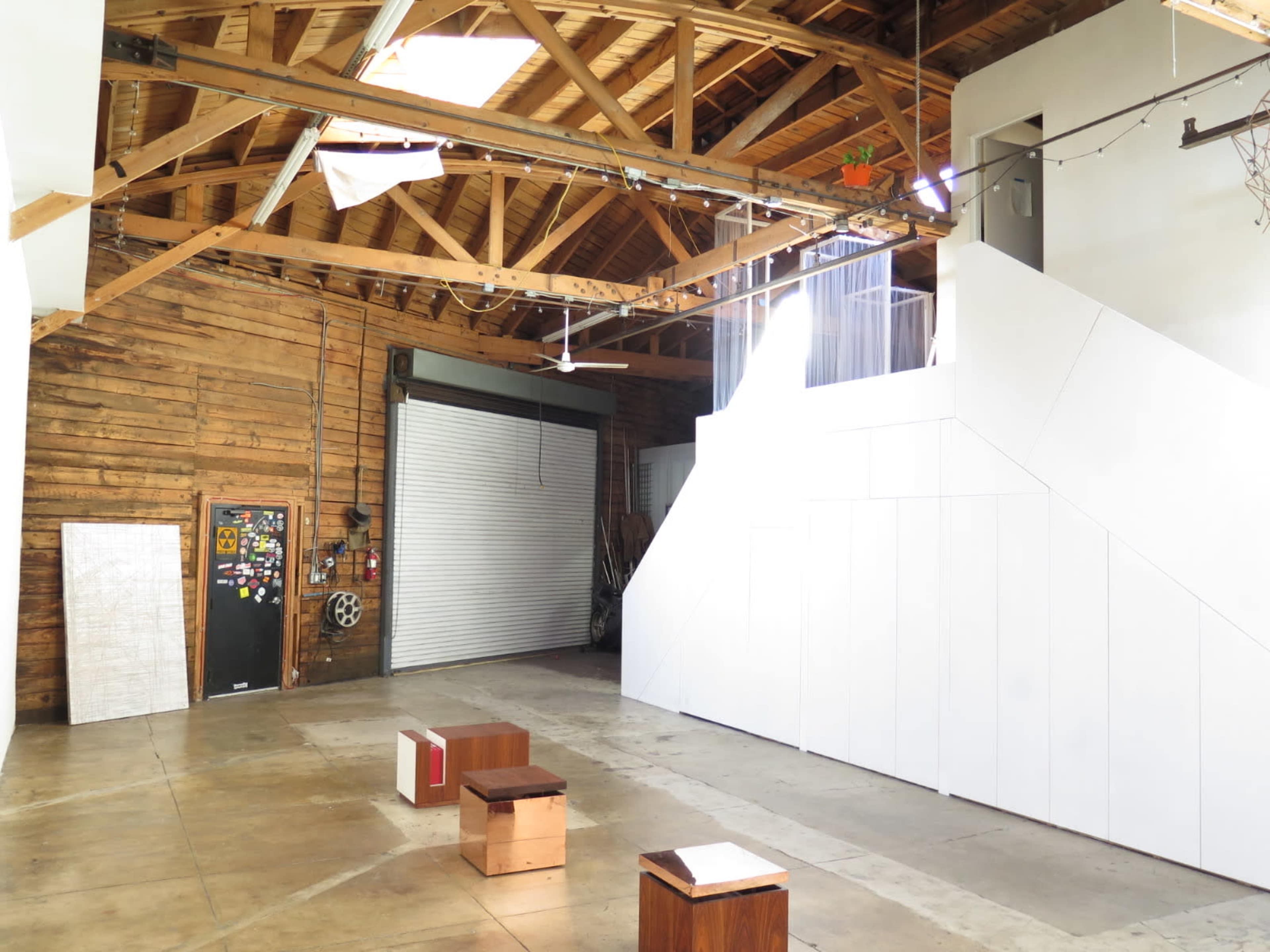 A spacious, industrial-style interior with wooden beams and a mix of white and brown surfaces, featuring benches and a large door at one end.