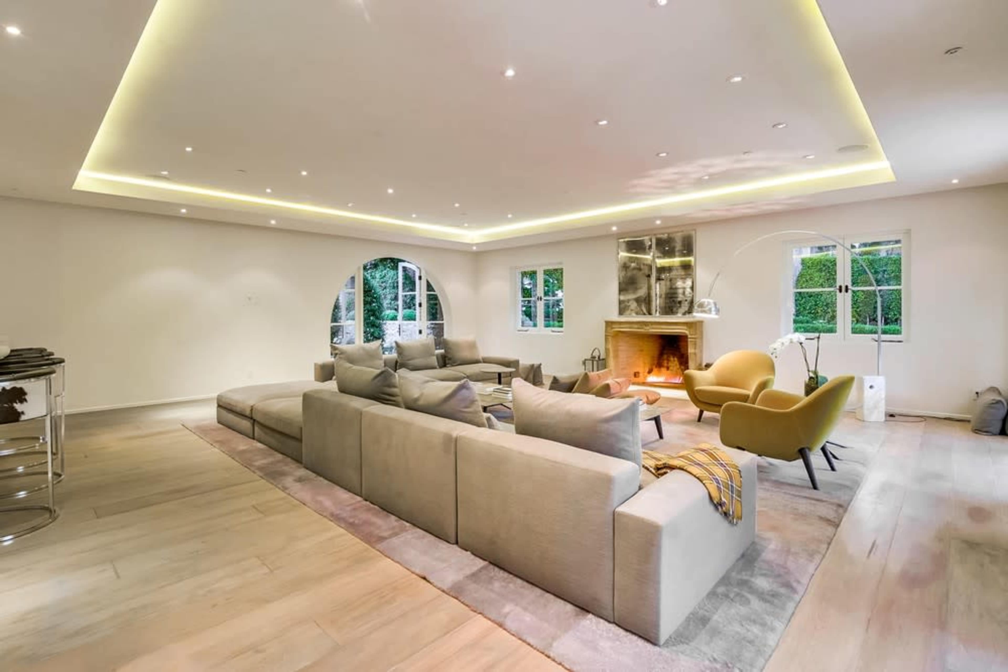 A spacious living room featuring a large sectional sofa, a fireplace, and a yellow armchair, illuminated by recessed lighting.