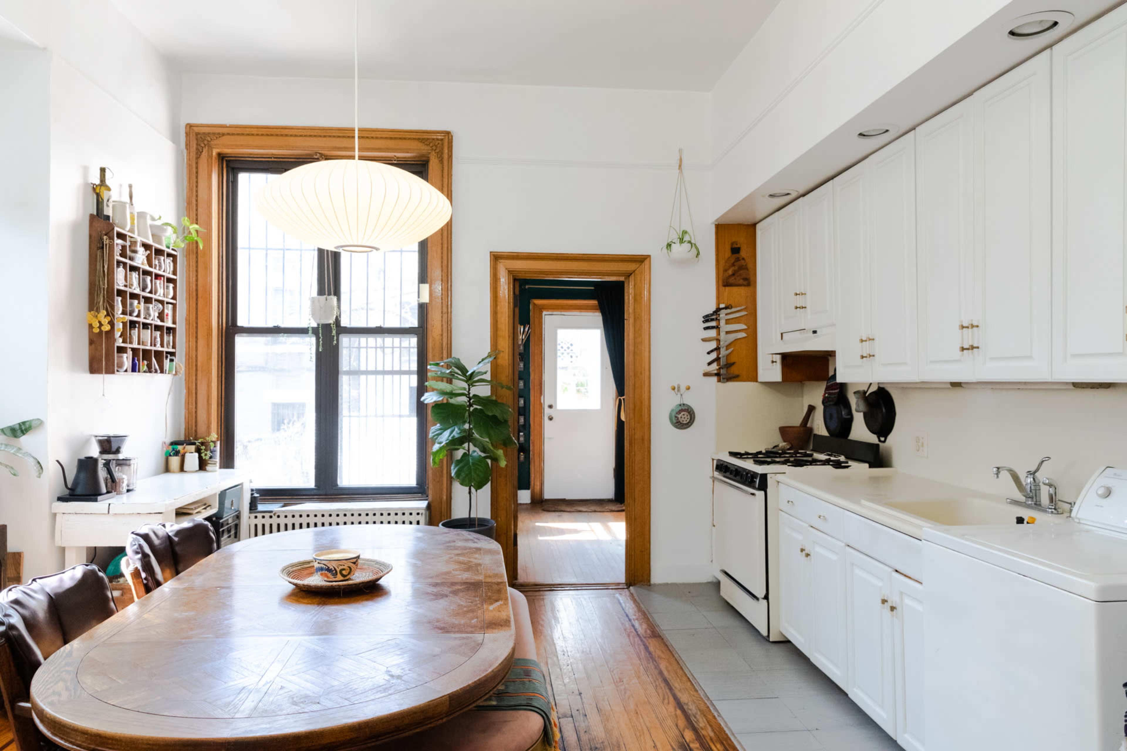 A well-lit kitchen features a wooden dining table, white cabinets, and a doorway leading to an outdoor space.
