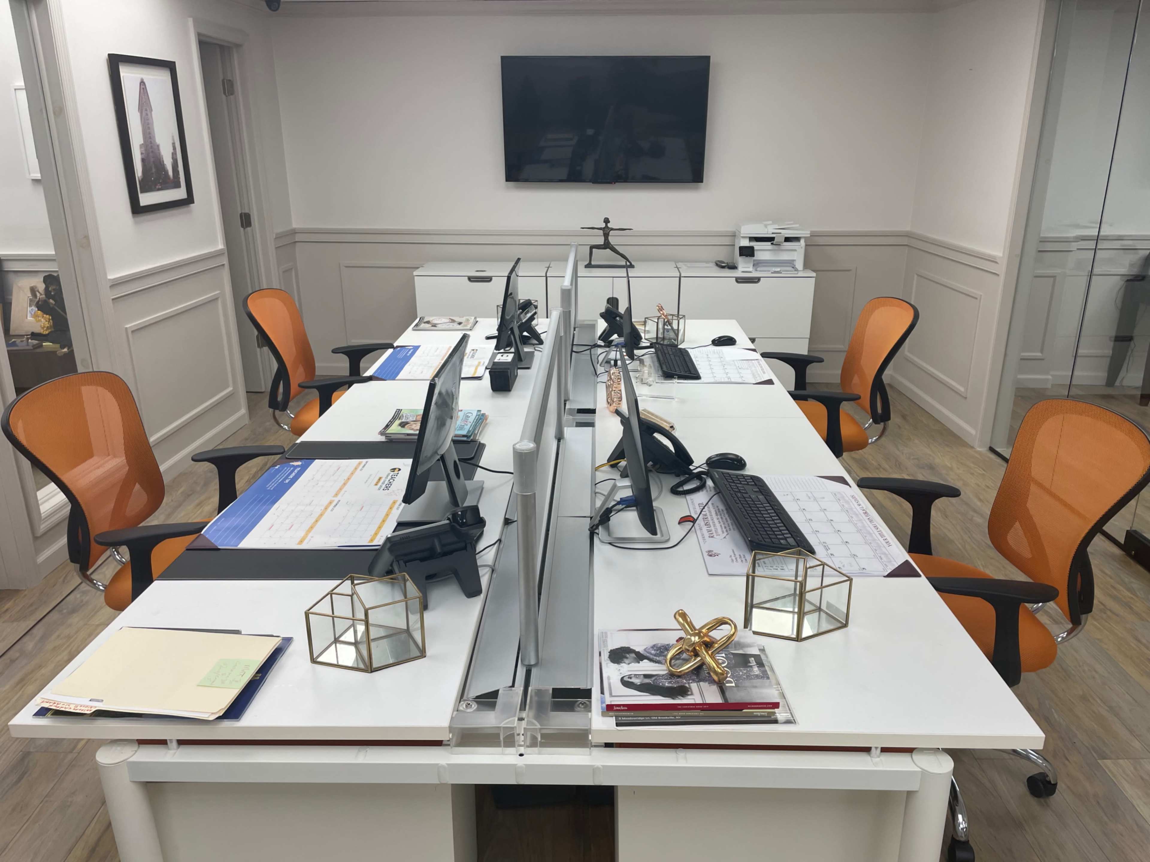 A modern office setup with two workstations facing each other, each equipped with computers and orange chairs.
