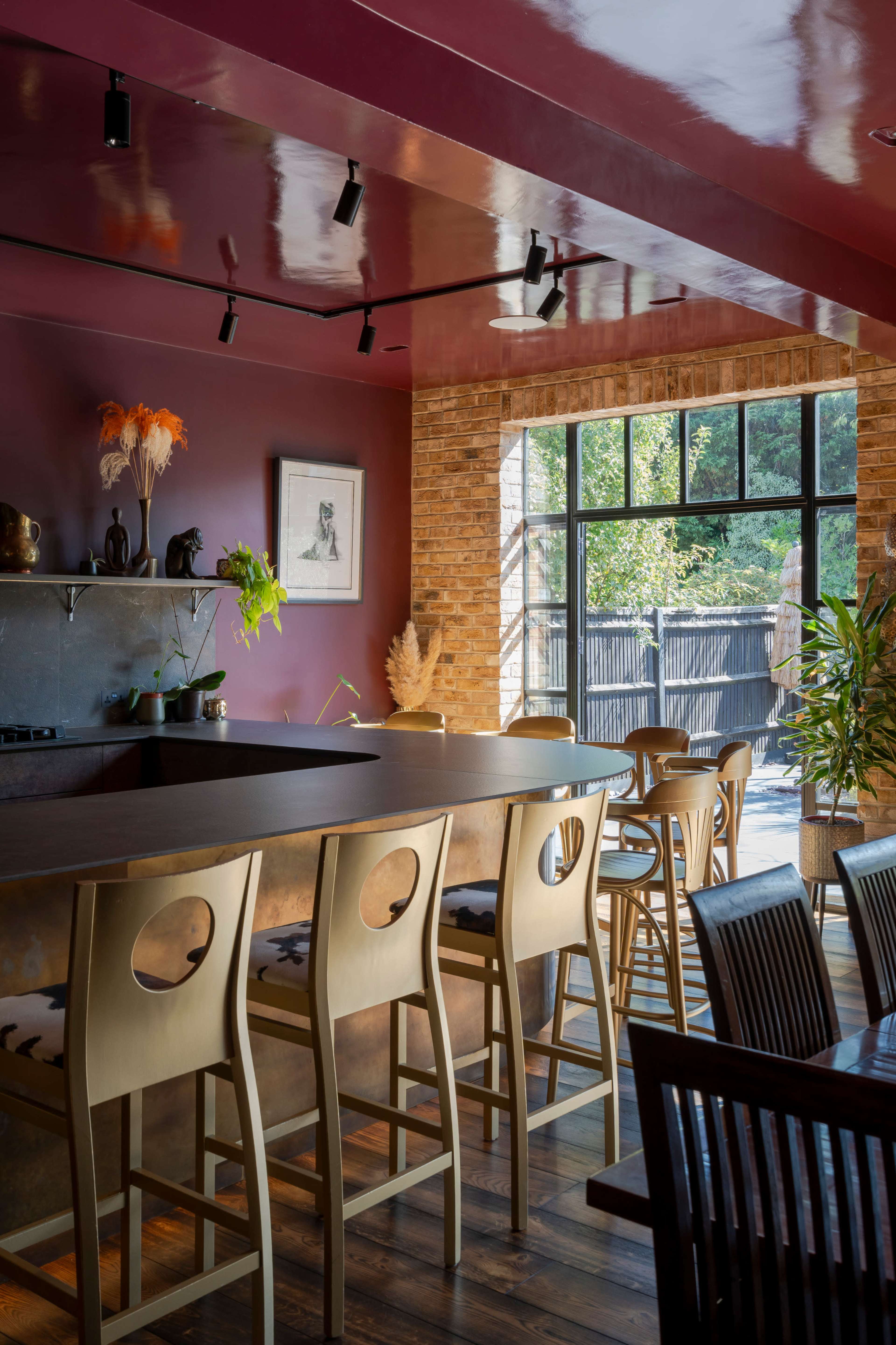 A modern bar area with a long counter and high stools, featuring exposed brick walls and large windows that overlook an outdoor space.