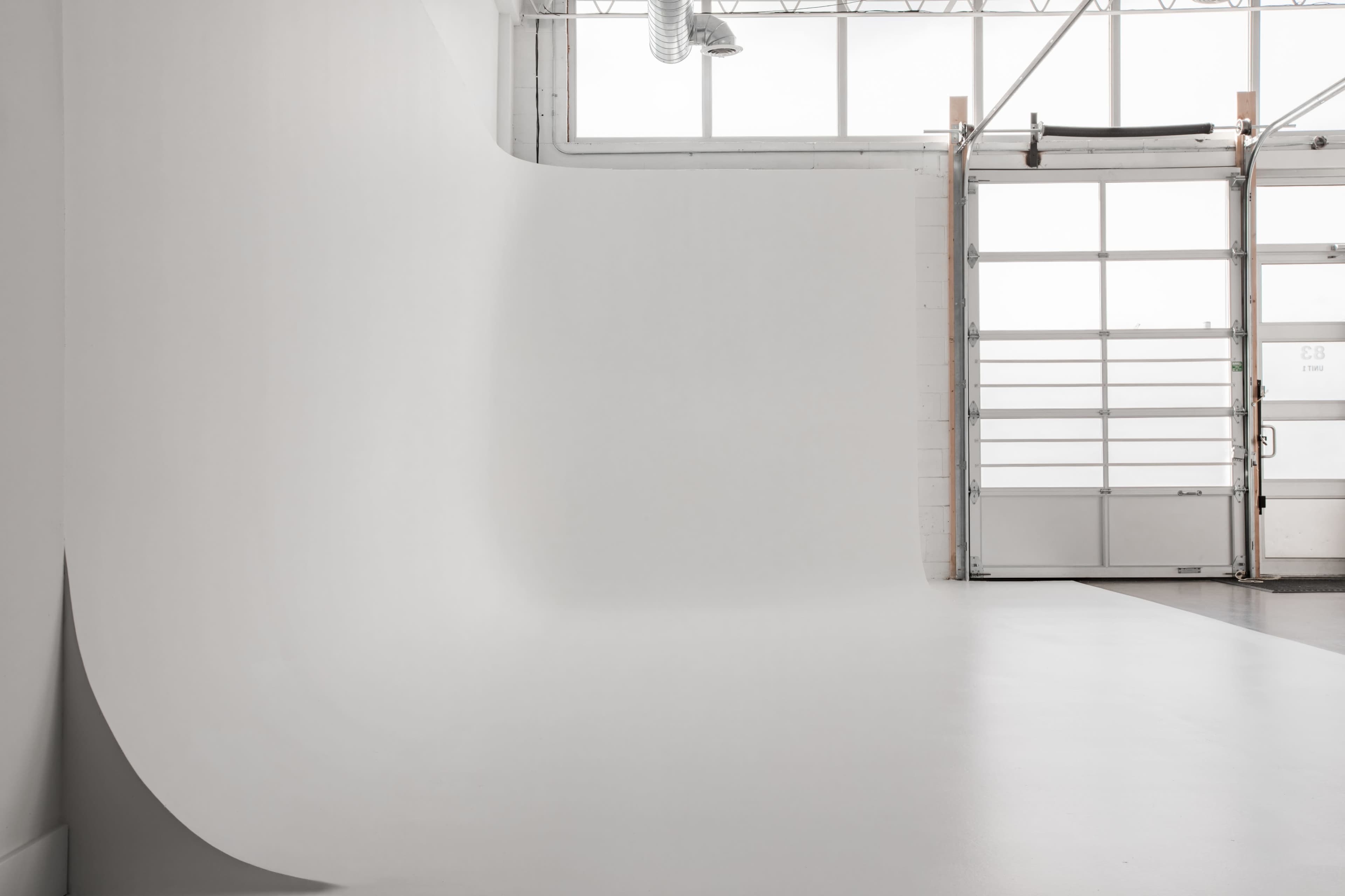 An empty studio space with a seamless white backdrop and large windows allowing natural light to enter.