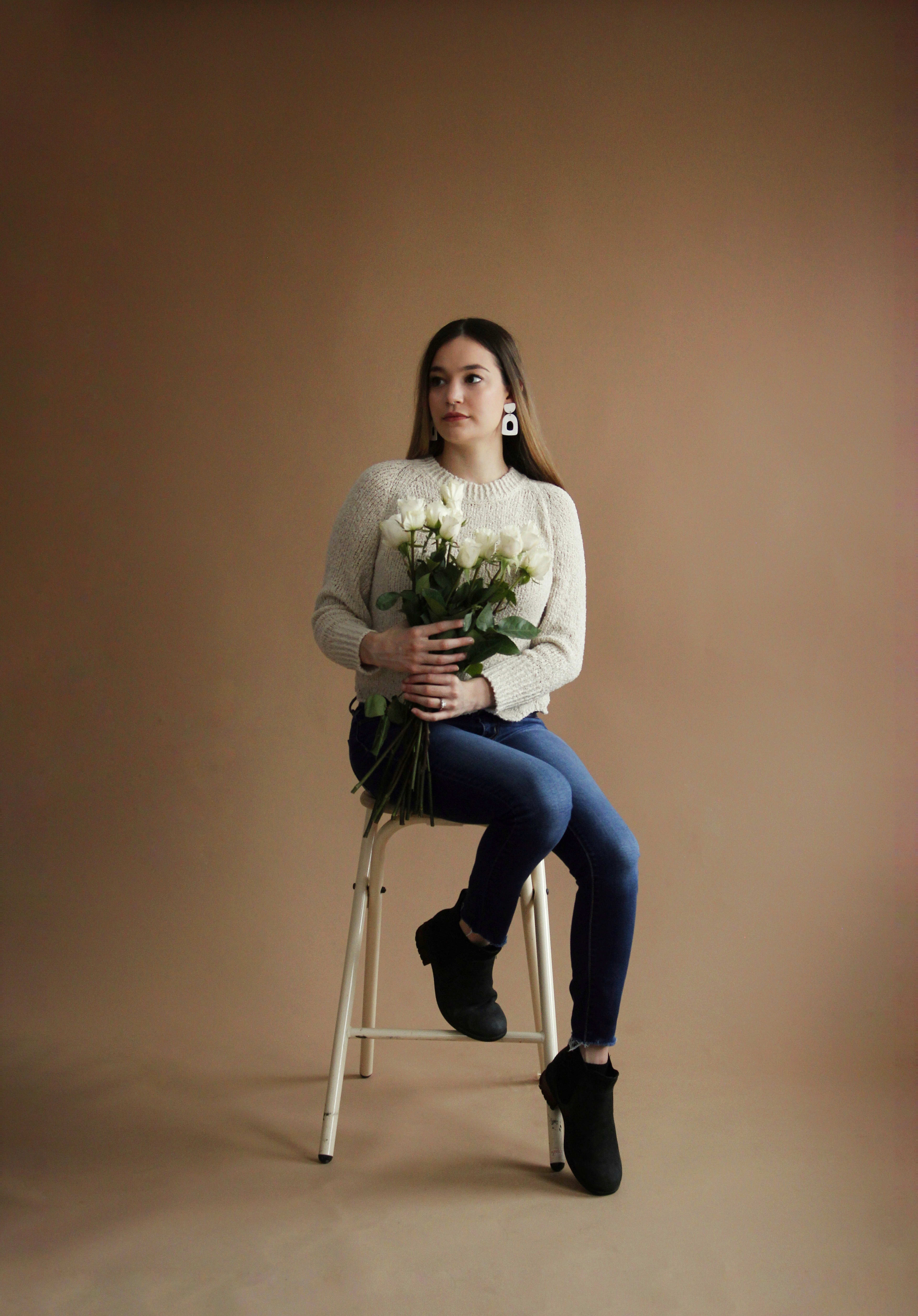 A portrait of a woman holding a bouquet of white roses on a stool.