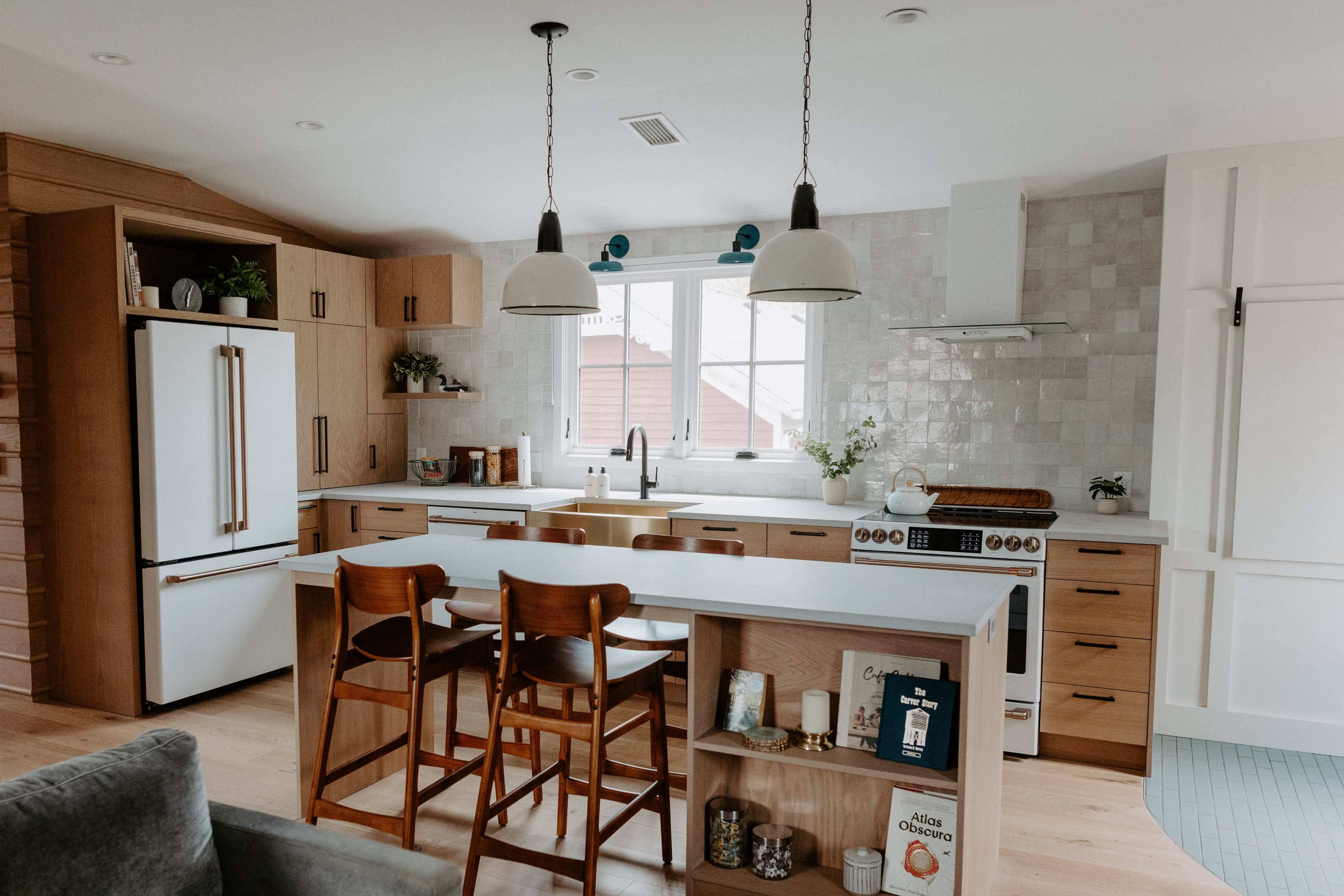 A modern kitchen features wooden cabinets, a large island with bar stools, and a window above the sink.