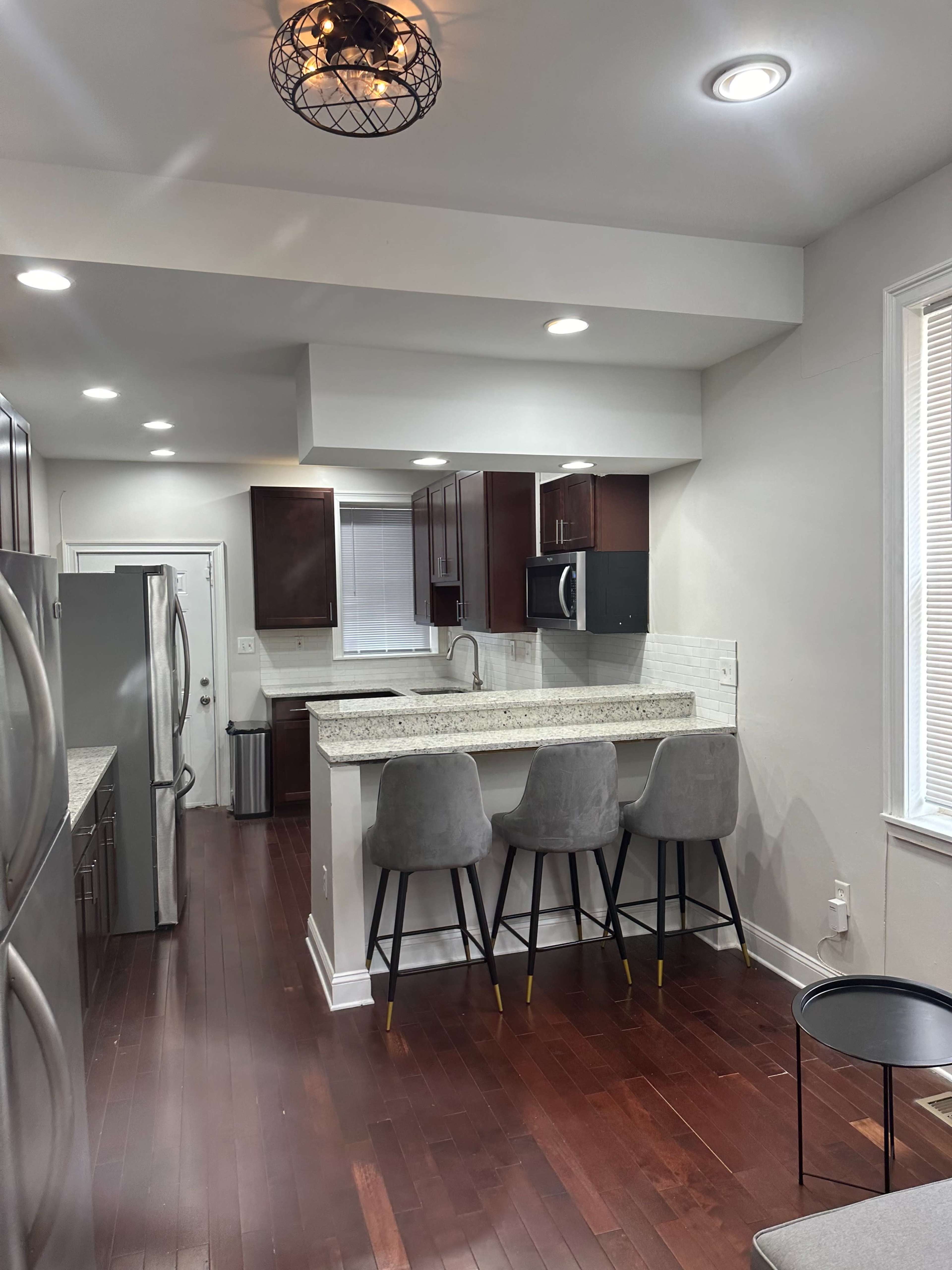 A modern kitchen with dark cabinetry, a white countertop, and three gray bar stools at a countertop island.
