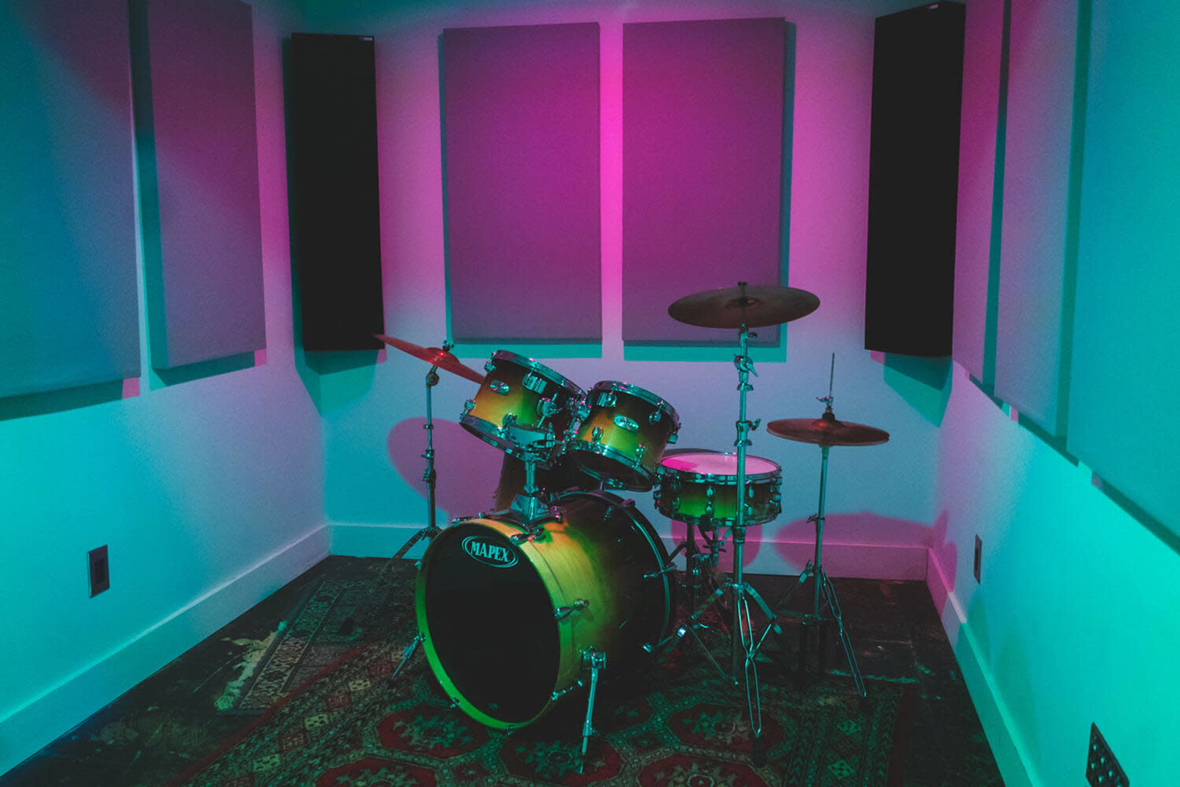 A drum set is positioned in a soundproofed room with colorful lighting and sound-absorbing panels on the walls.