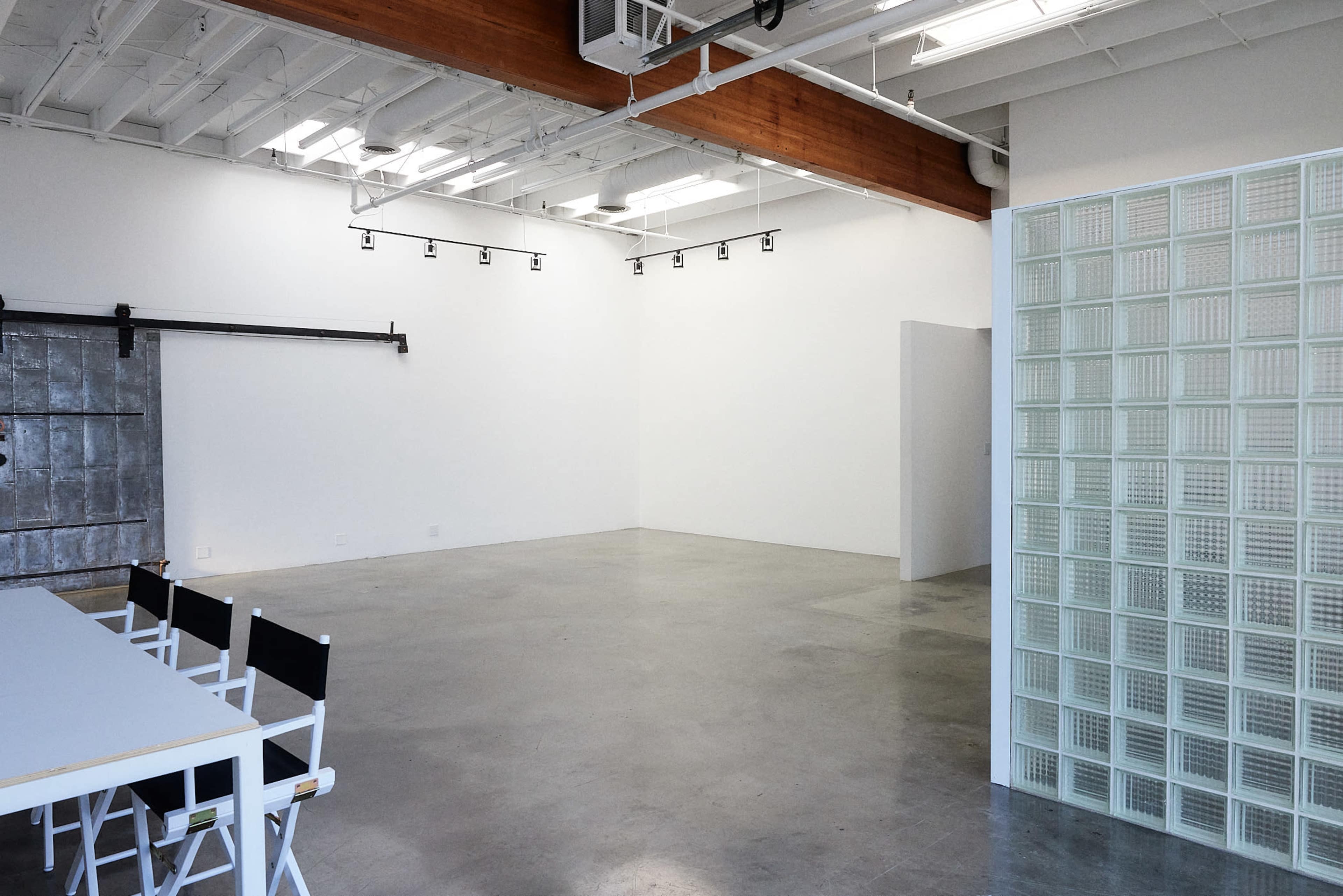 An empty gallery space with polished concrete floors, exposed beams, and a glass block wall on one side.
